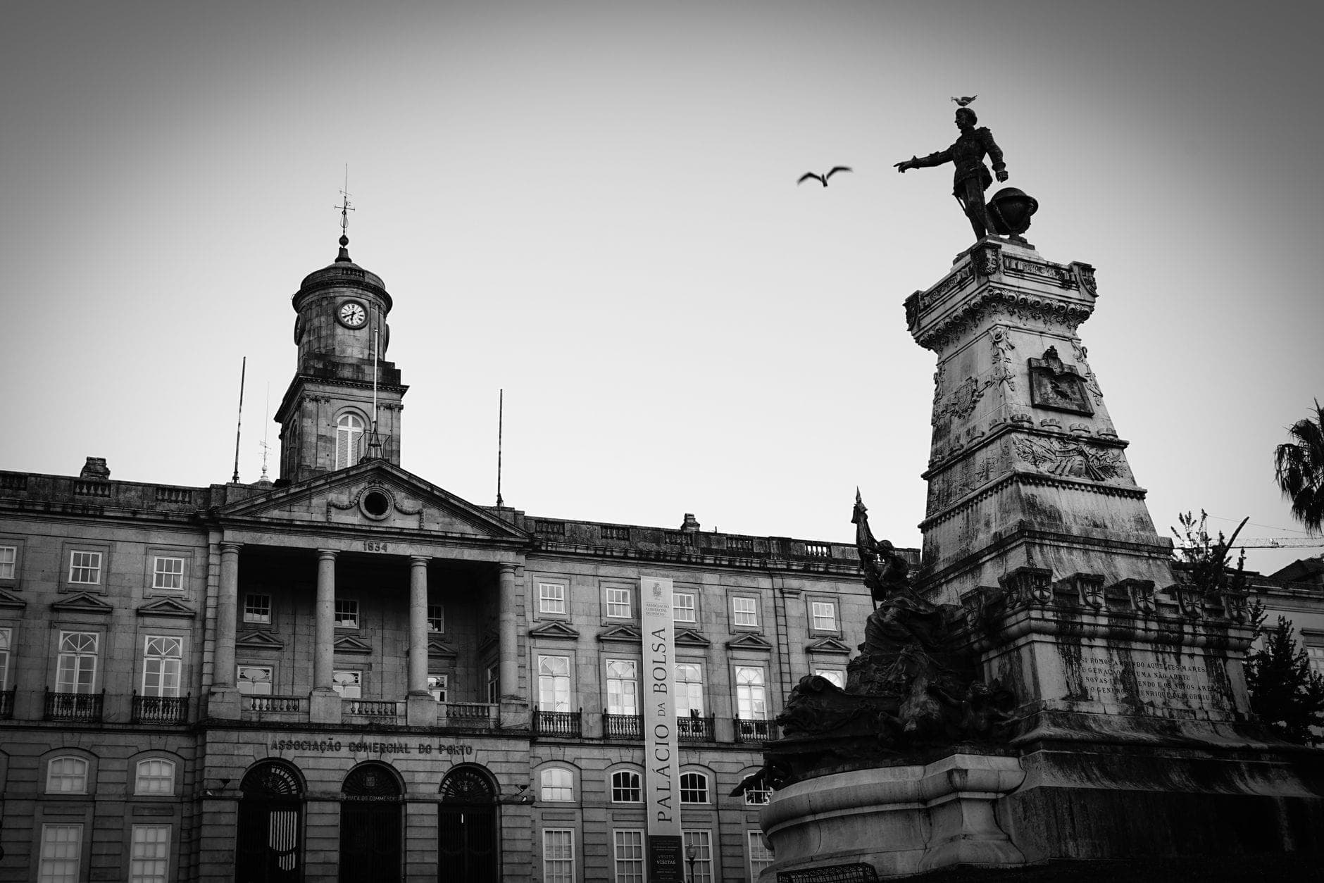 Schwarz-Weiß-Aufnahme der neoklassizistischen Fassade des Palácio da Bolsa mit einer markanten Statue und einem Uhrenturm in Porto, Portugal.