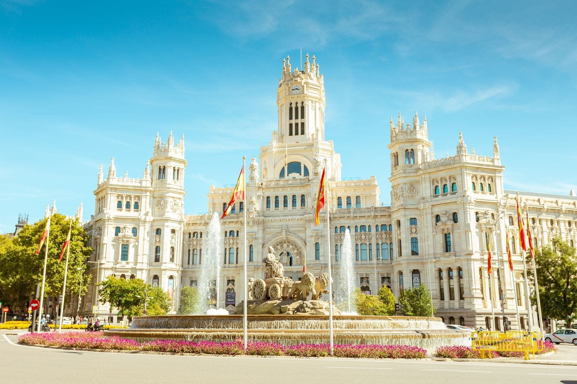 Palacio de Cibeles ใจกลางมาดริด ในวันที่ฟ้าใส แดดออก มีธงสเปนและน้ำพุ Cibeles อยู่ด้านหน้า