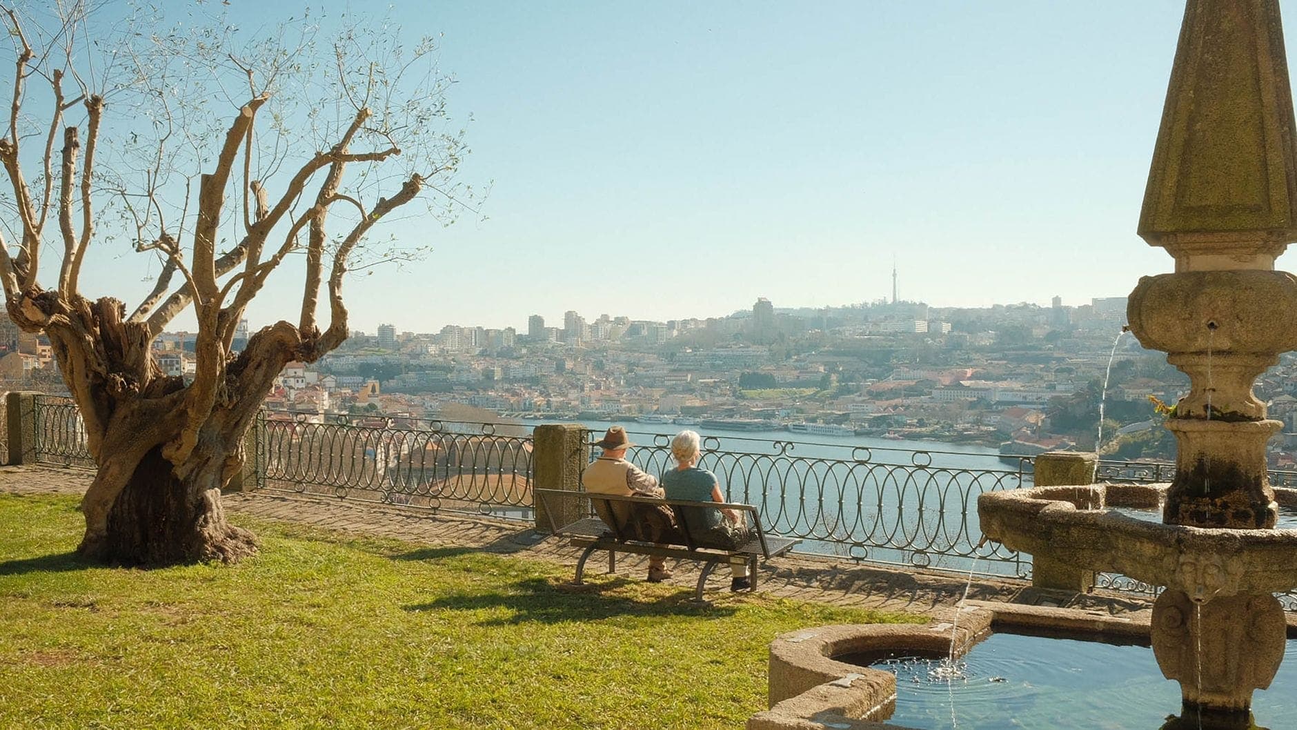 Zwei Menschen sitzen auf einer Bank in den Jardins do Palácio de Cristal und blicken auf den Douro – mit Panoramaaussicht auf Porto und einem klassischen Gartenbrunnen im Vordergrund.