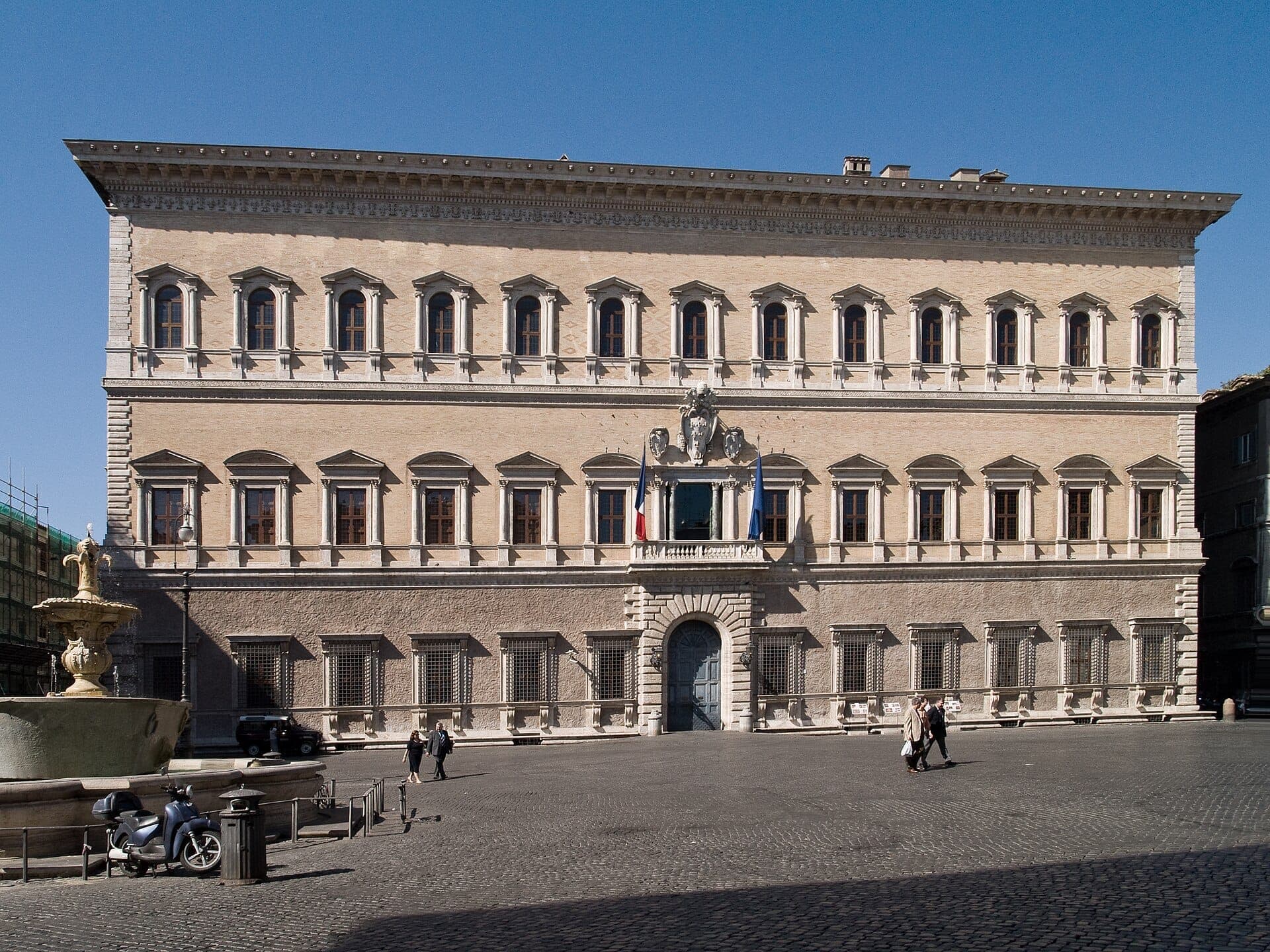 Harapang tingin ng Palazzo Farnese sa Roma, na nagpapakita ng Renaissance na arkitektura, simetrикong mga bintana, mga bandilang Pranses, at mga taong naglalakad sa maliwanag na piazza.