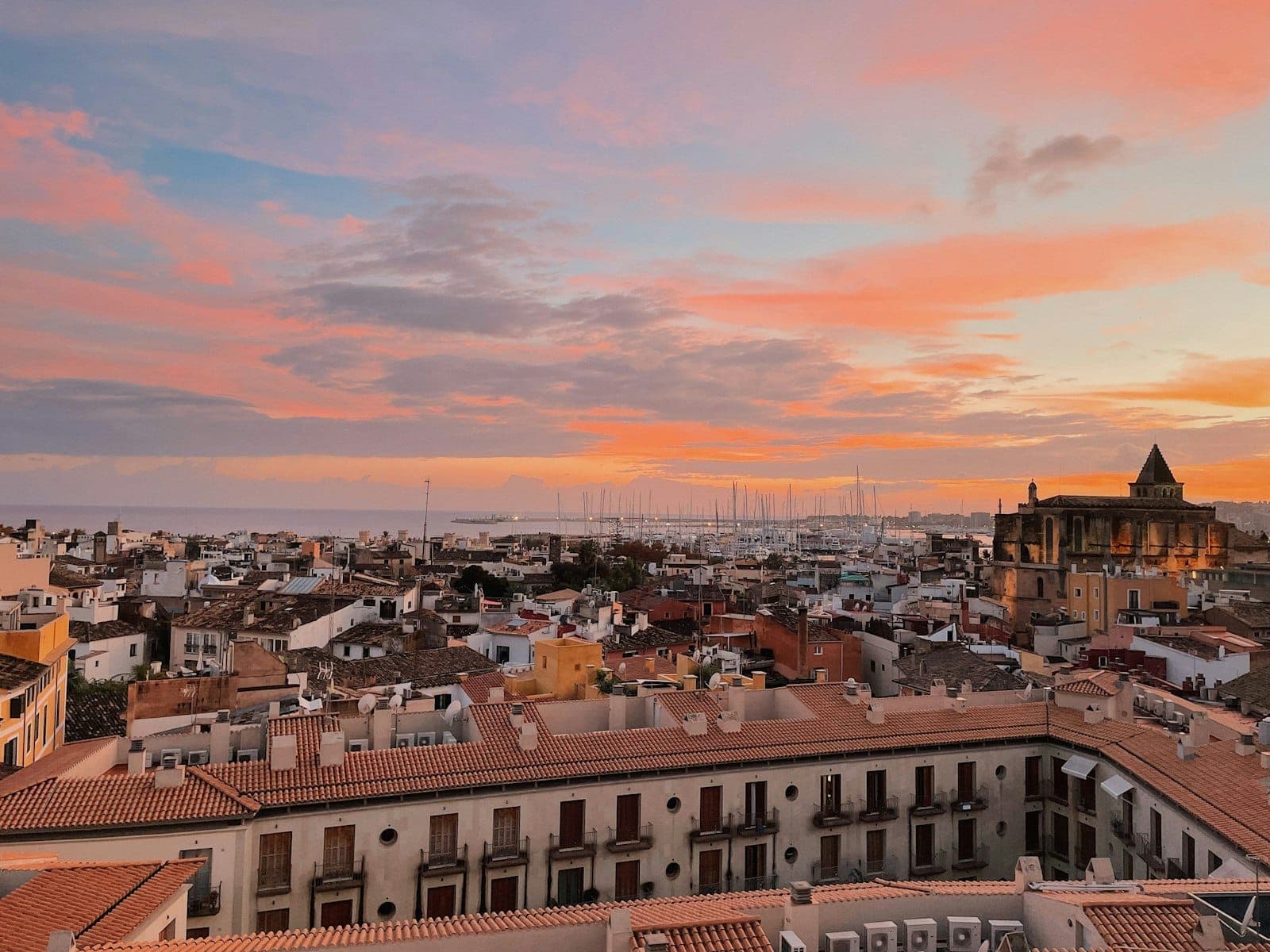 Panoramablick über die Altstadt von Palma de Mallorca mit terrakottafarbenen Dächern, der gotischen Kathedrale, der Marina und einem farbenprächtigen Sonnenuntergangshimmel über der Stadt.