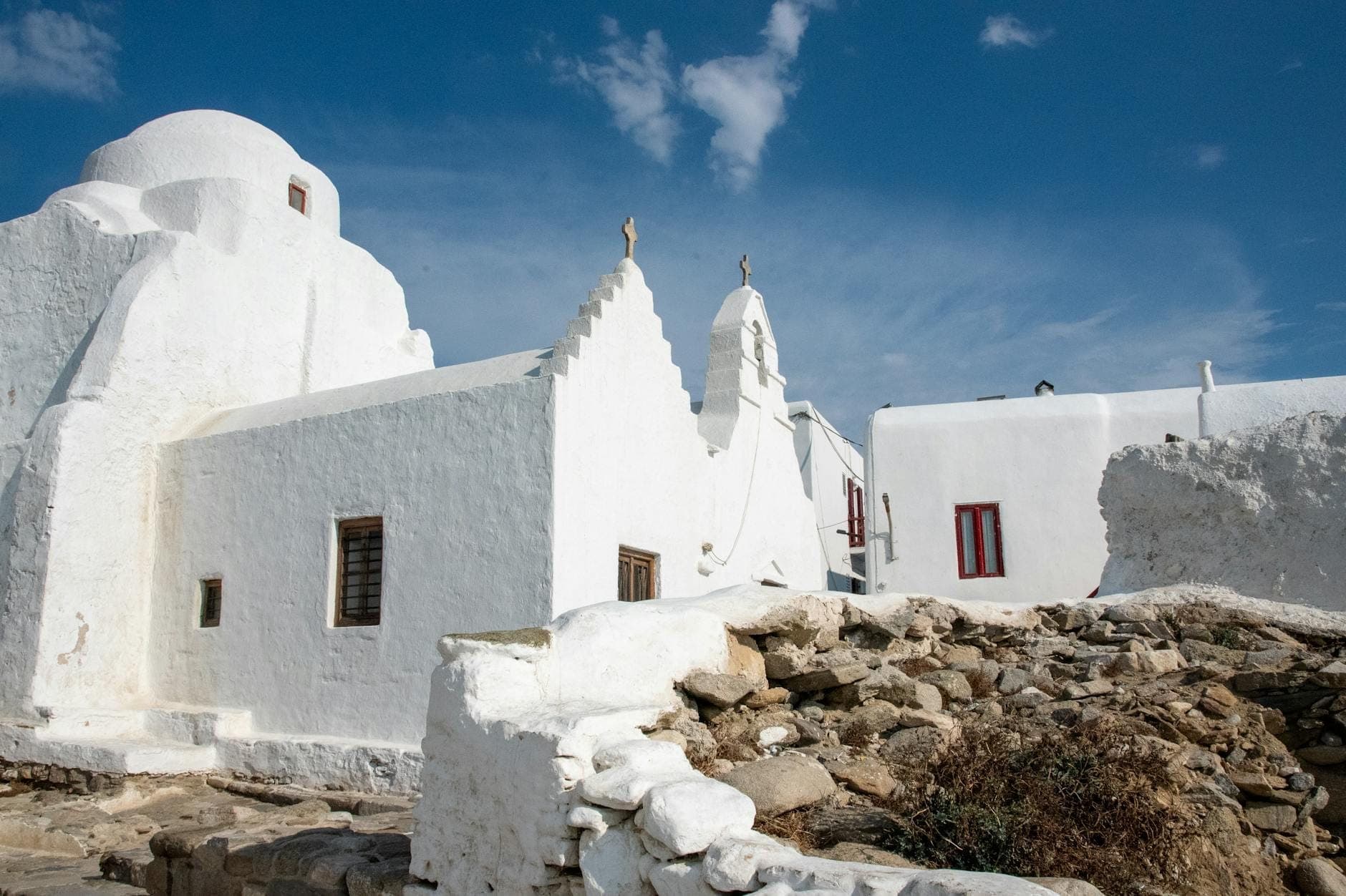 Weitwinkelperspektive auf das weiß getünchte, asymmetrische Äußere der Panagia Paraportiani mit ihren markanten Formen unter einem strahlend blauen Himmel auf Mykonos, Griechenland.