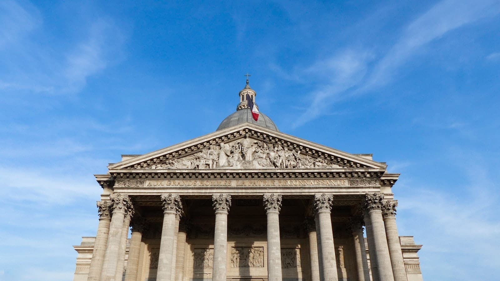 Front view of the Panthéon in Paris with its neoclassical columns and dome beneath a blue sky, captured in landscape orientation.