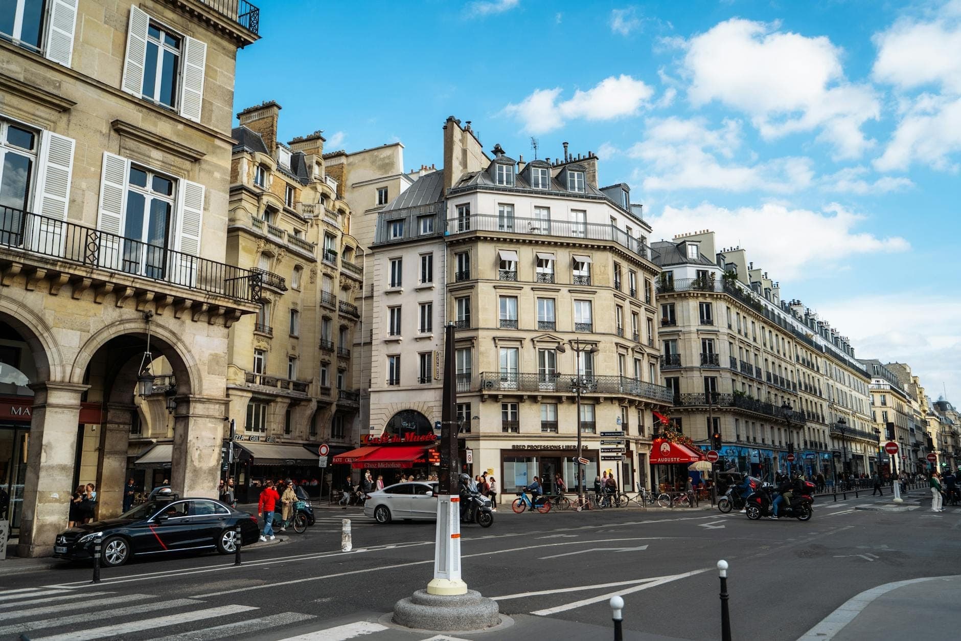 Cảnh phố với những tòa nhà Paris cổ điển, quán cà phê và người đi bộ trong một khu trung tâm sầm uất vào một ngày nắng đẹp.