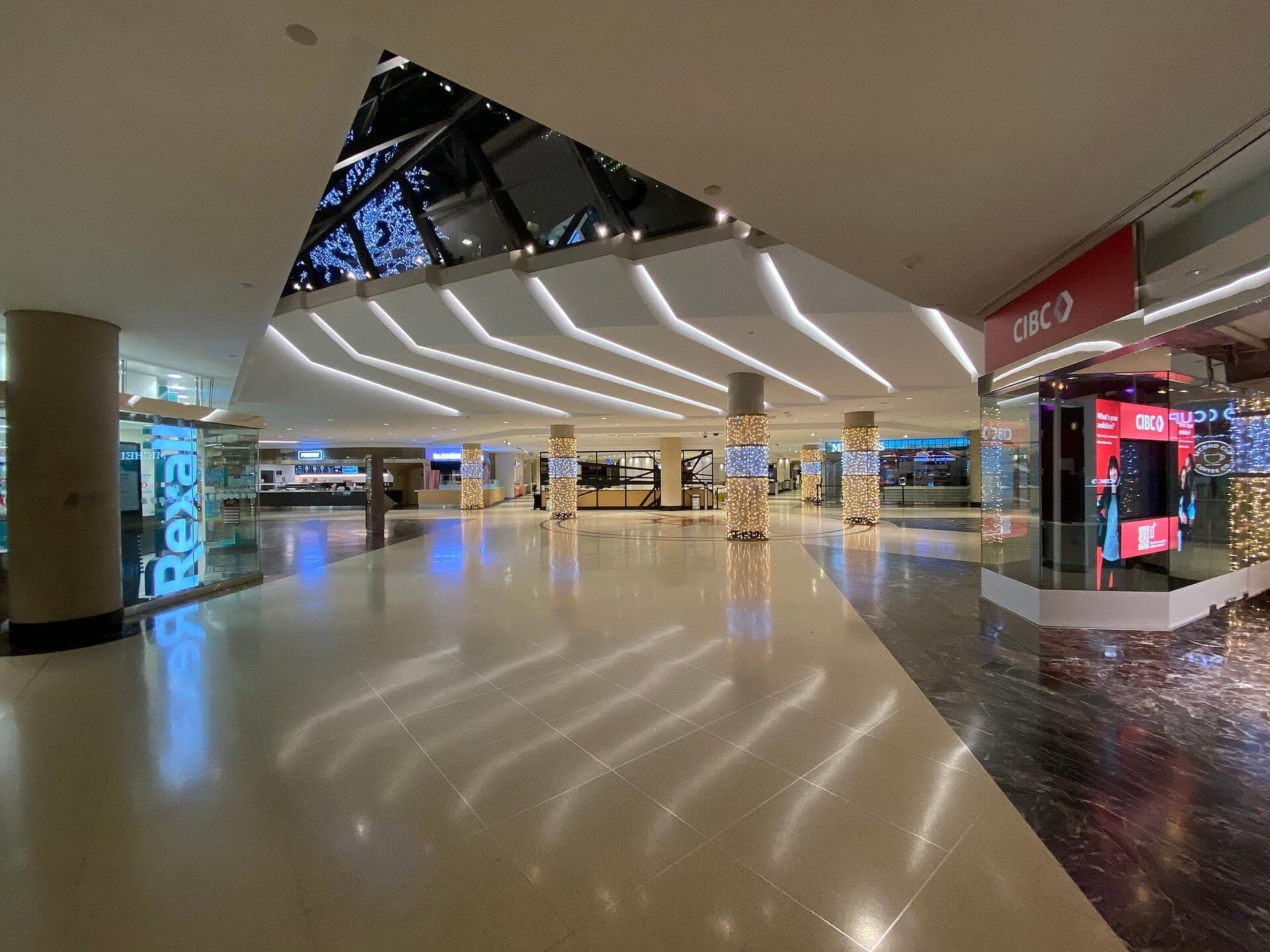 Ampio e moderno corridoio all'interno della PATH Underground City di Toronto, con illuminazione intensa, pilastri illuminati, vetrine in vetro e segnaletica bancaria.