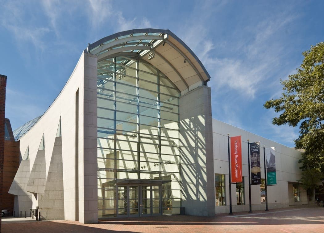 Entrée moderne en verre et pierre du Peabody Essex Museum à Salem, Massachusetts, avec des bannières et un ciel bleu en arrière-plan.