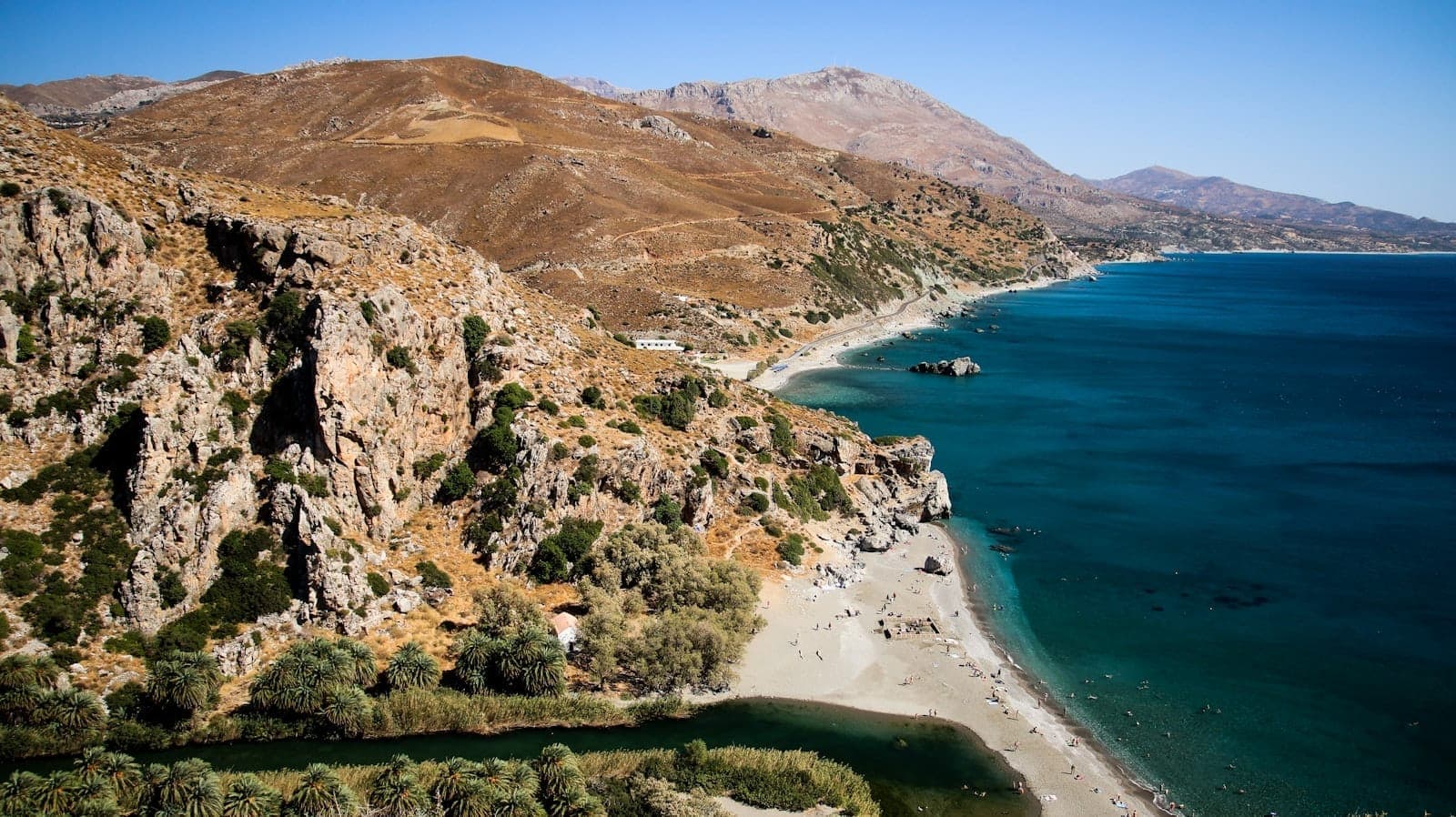Vue aérienne de Pefkos Beach montrant du sable doré, une mer turquoise, des falaises rocheuses et des baigneurs éparpillés sous un ciel bleu dégagé.