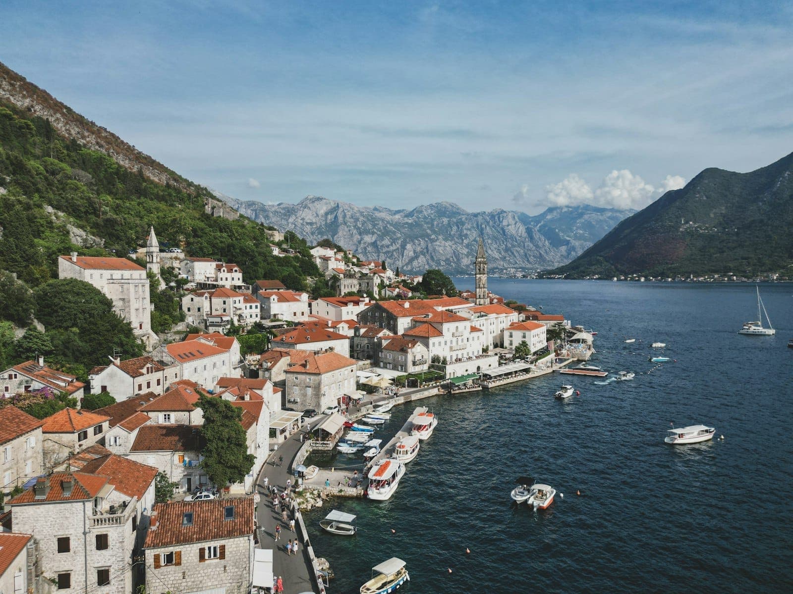 Vue saisissante du front de mer de Perast avec ses bâtiments baroques aux toits rouges, des barques amarrées le long du quai et des montagnes impressionnantes se dressant derrière le village sur la baie de Kotor.