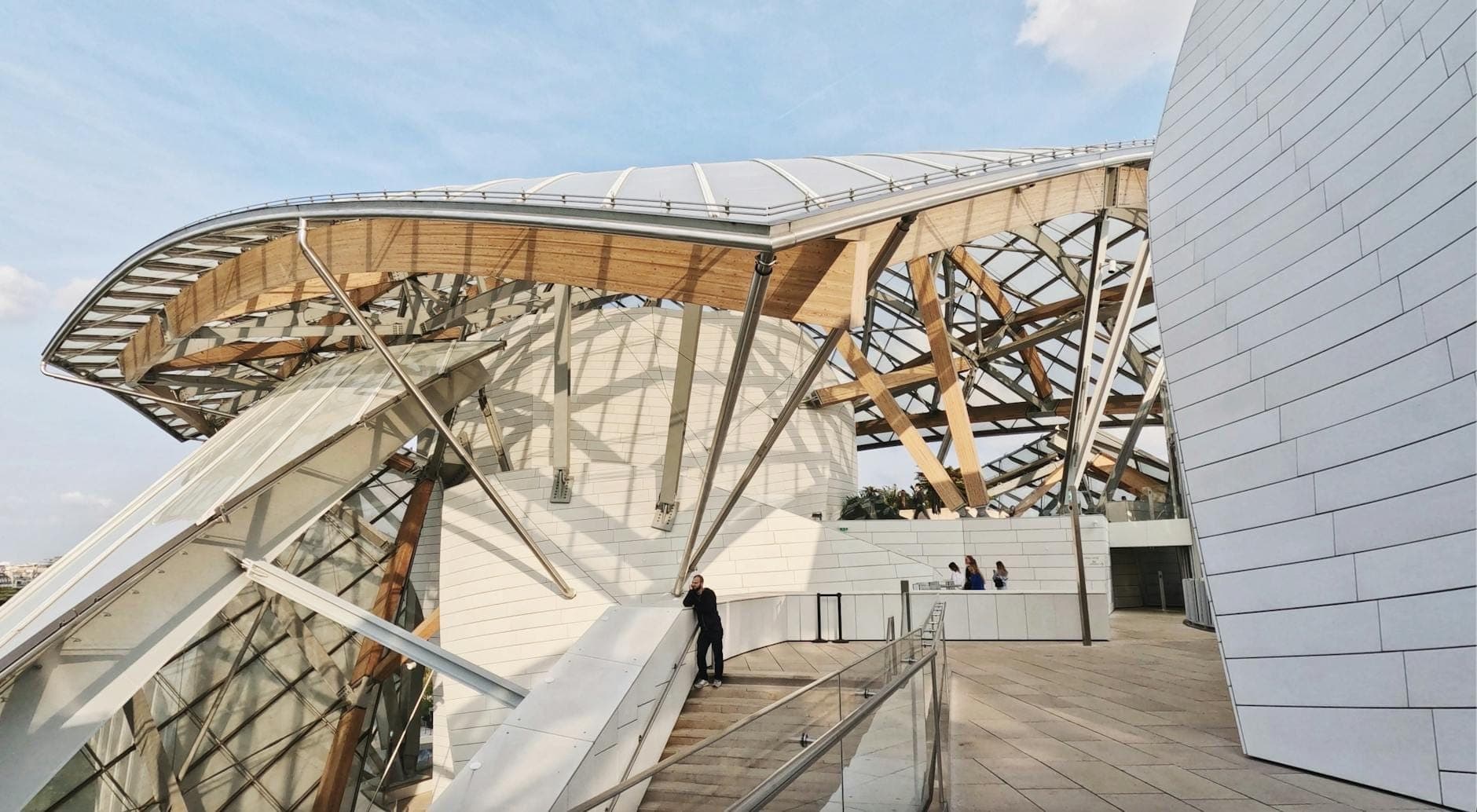 Wide view of the modern Philharmonie de Paris building with glass and metal curves, showing bold architecture and visitors on the terrace.