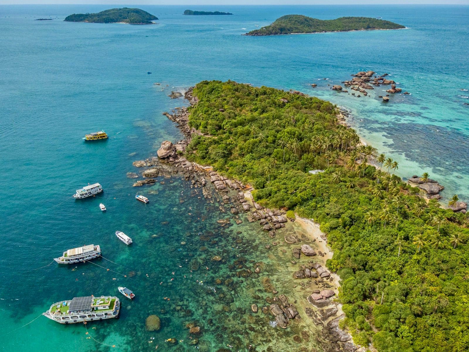 Cảnh nhìn từ trên cao của hòn đảo xanh mướt với những chiếc thuyền neo đậu ngoài khơi trên làn nước xanh ngọc trong vắt, đặc trưng của Phú Quốc trong thời tiết yên bình mùa khô.