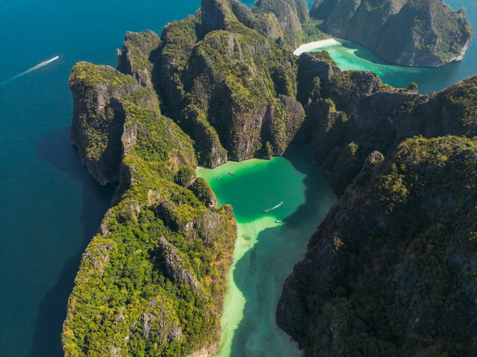 Aerial na tingin ng mga dramatikong limestone na isla at turquoise na tubig ng lagoon, katangian ng mga isla ng Phi Phi malapit sa Phuket, na may mga bangka sa look.