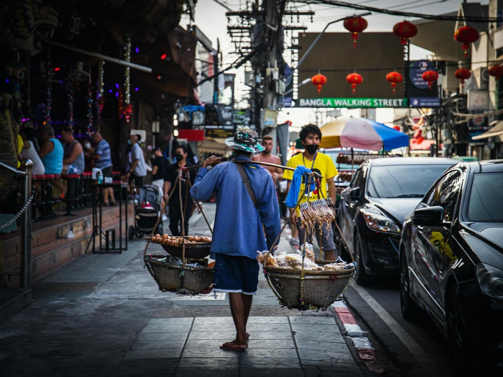 บรรยากาศถนนบางลาในภูเก็ตยามเย็น พร้อมหาบเร่แบกอาหารและป้าย Bangla Walking Street เหนือศีรษะ