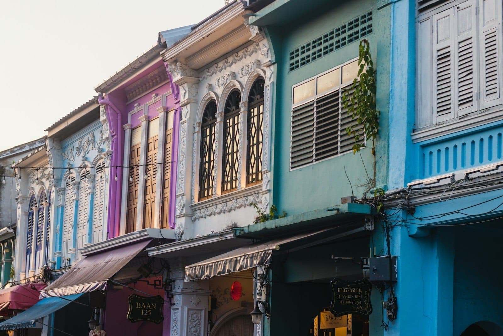 Colorful Sino-Portuguese shophouses with ornate arched windows and pastel facades in Phuket Old Town, captured in warm daylight along the historic street.