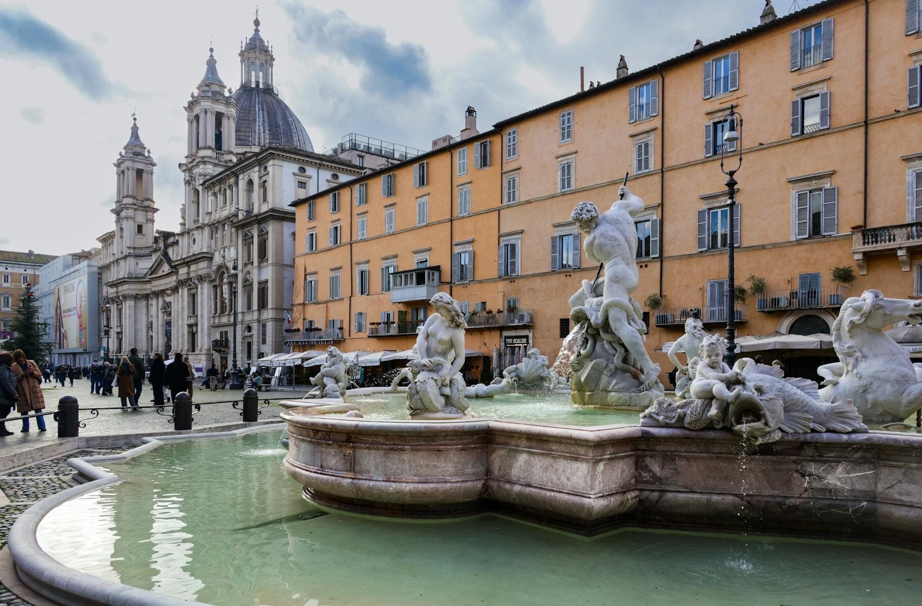 Malawak na tanawin ng Piazza Navona na may mga sikat nitong Baroque na bukal, mahahabang eskultura, mga simbahanang may gusali, at napapaligiran ng mga gusaling kulay oker sa ilalim ng dramatikong langit habang naglalakad ang mga bisita sa parisukat.