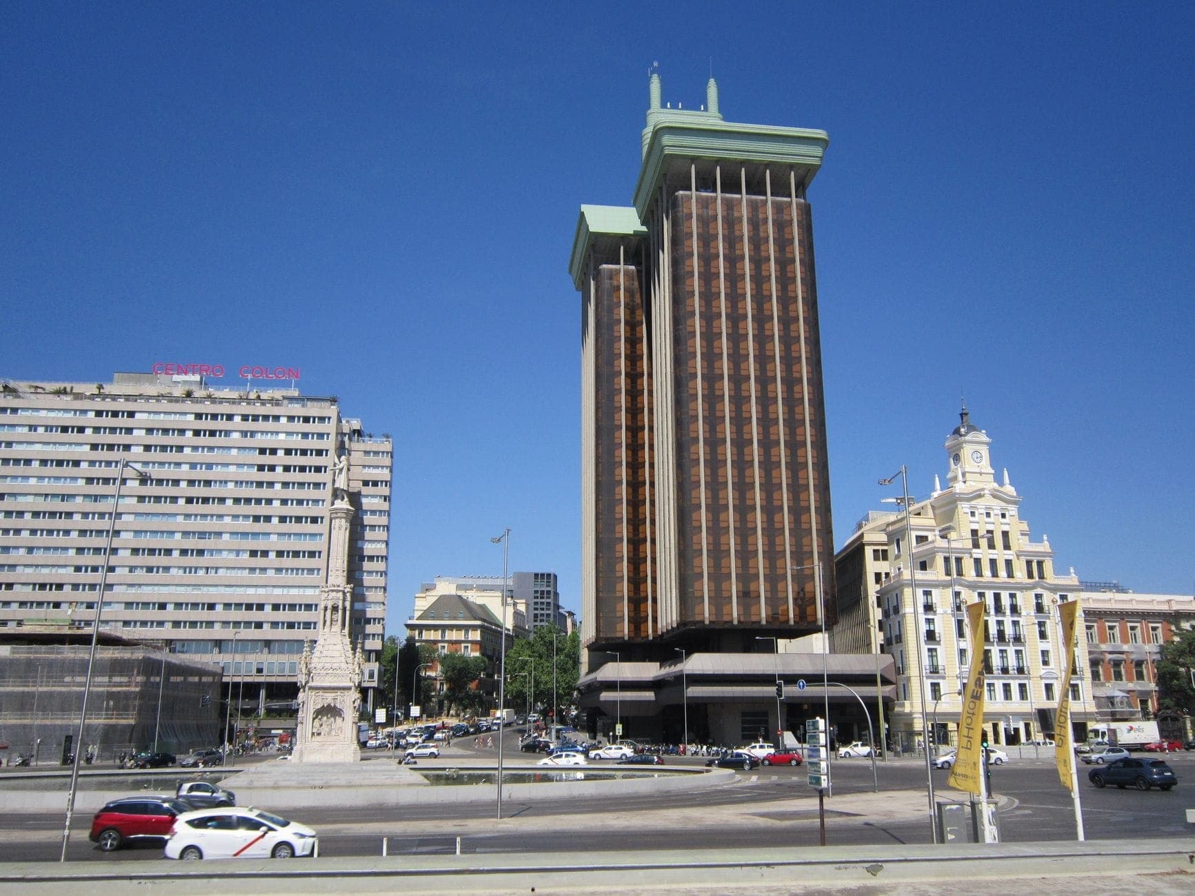 ภาพมุมกว้างของ Plaza de Colón ในมาดริด เห็นอนุสาวรีย์โคลัมบัส ตึกสูงสมัยใหม่ อาคารรอบด้าน และจัตุรัสเปิดโล่งใต้ท้องฟ้าสีคราม