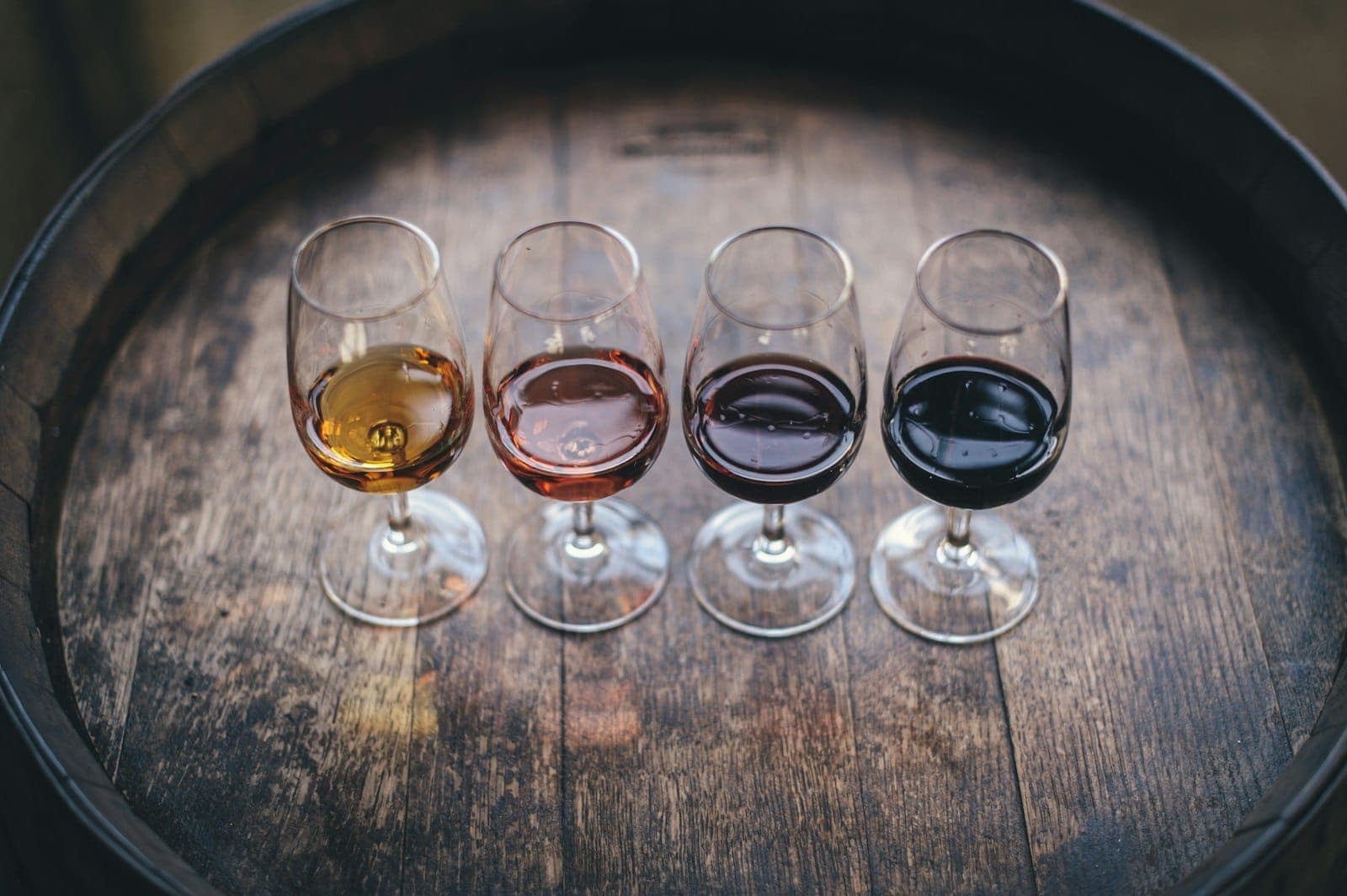 Quattro calici di vinho do porto di colori diversi disposti su una botte di legno, che rappresentano una degustazione a Porto.
