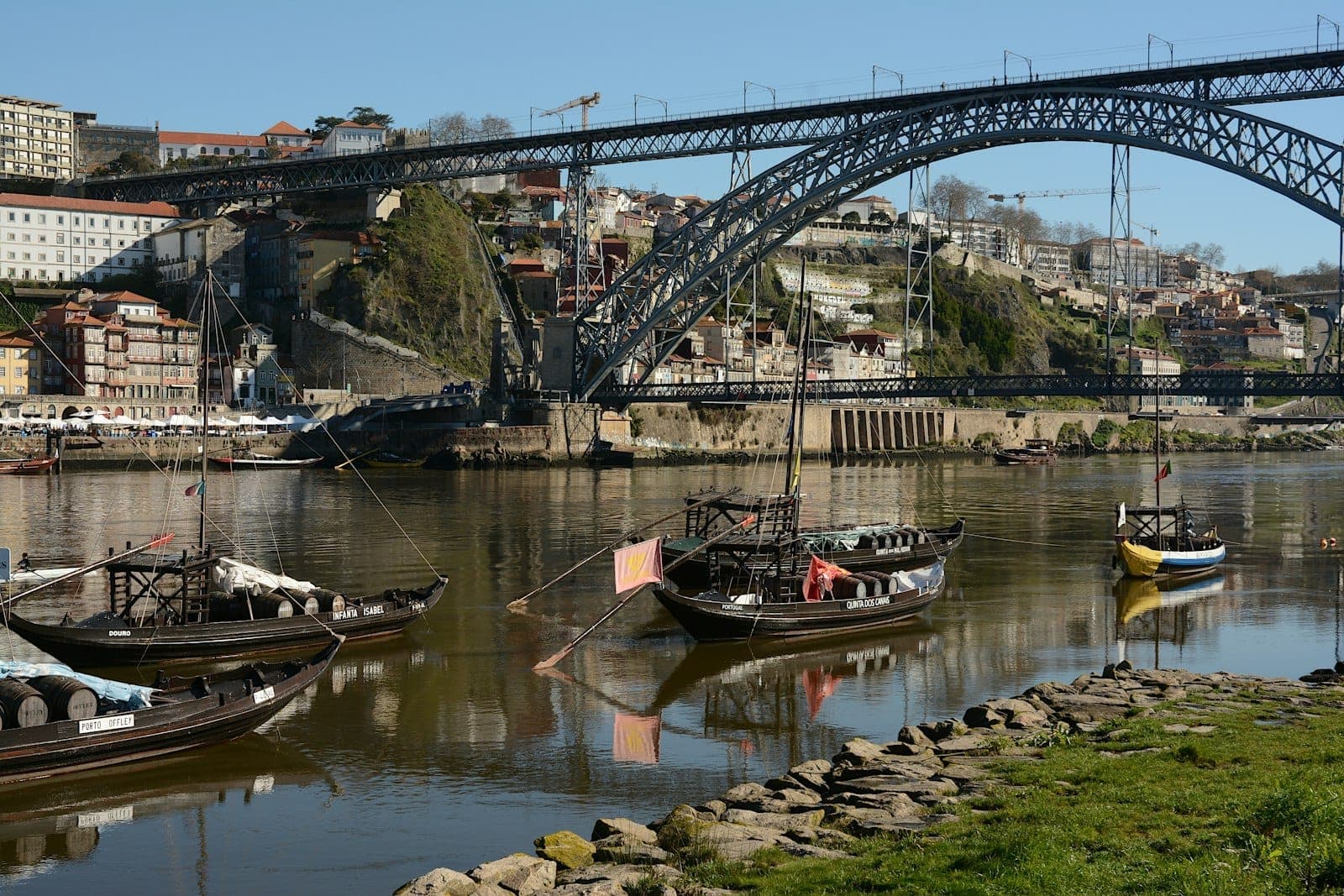 Barche rabelo sul fiume Douro davanti al ponte Dom Luís I, con le cantine di Gaia e gli edifici di Porto sullo sfondo.