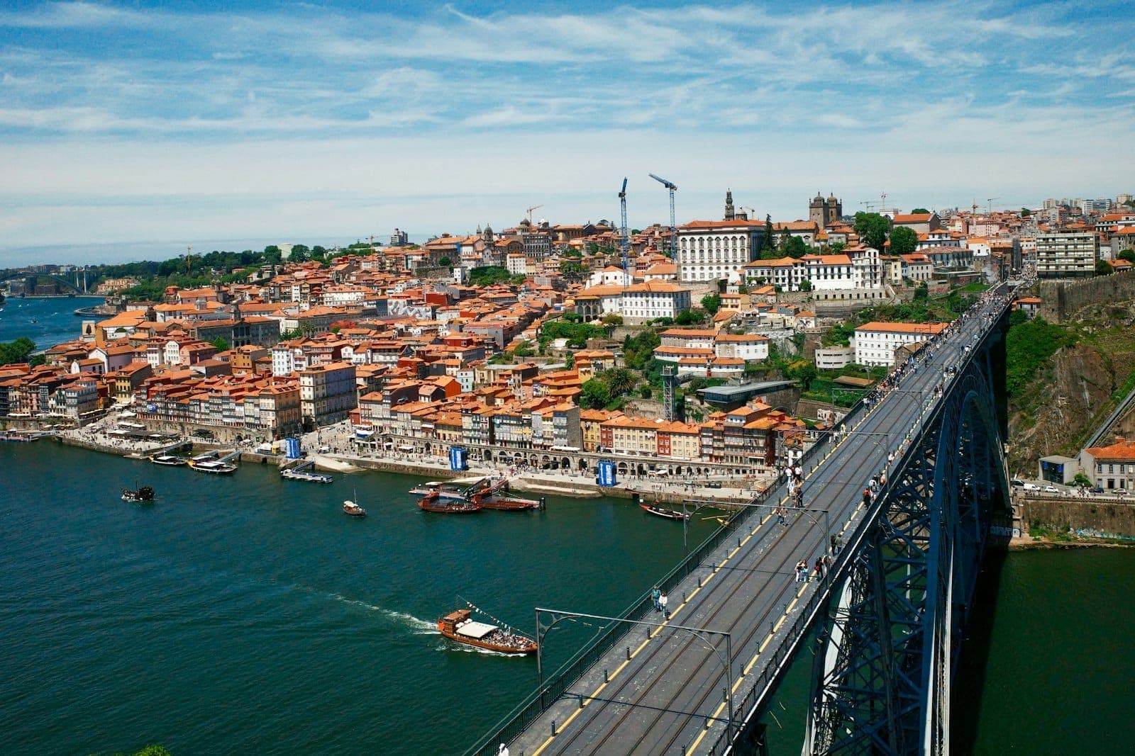 มุมมองทางอากาศของสะพาน Dom Luís I ที่ทอดข้ามแม่น้ำโดรู พร้อมย่าน Ribeira อันสีสันสดใสของปอร์โตที่เรียงรายอยู่ริมแม่น้ำภายใต้ท้องฟ้าสีฟ้าสดใส