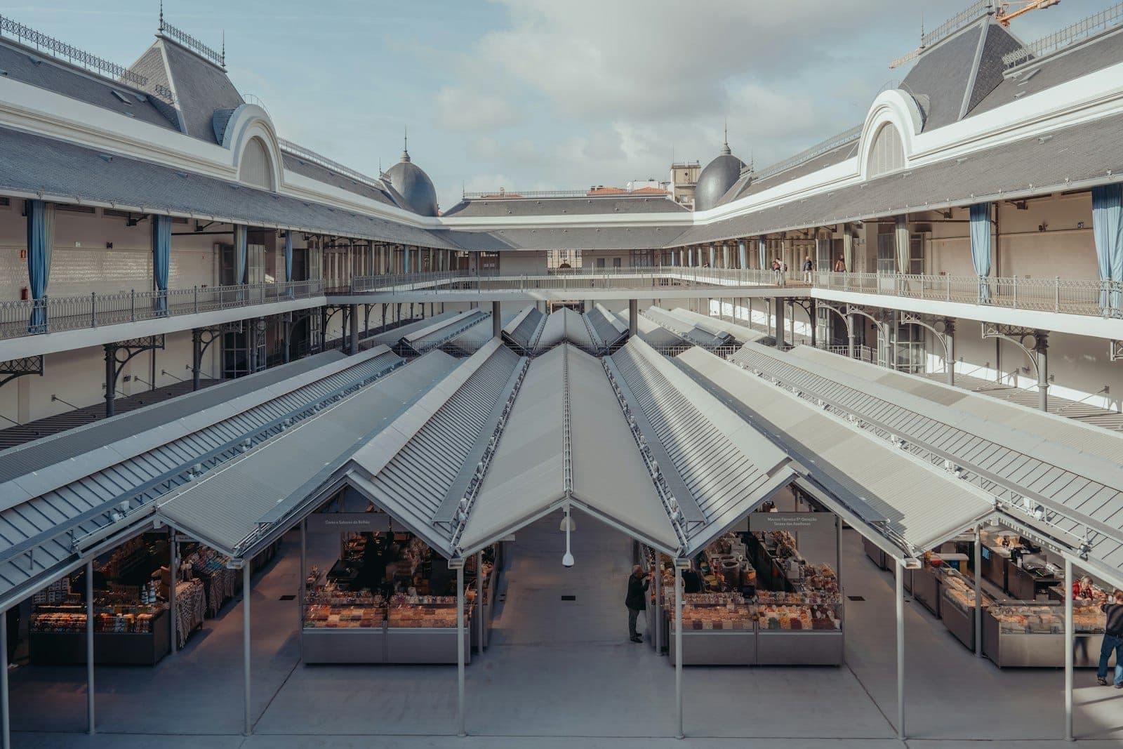 มุมมองกว้างของภายในตลาด Mercado do Bolhão ที่ได้รับการปรับปรุงใหม่ พร้อมแผงขายของที่สว่างสดใส หลังคากระจก และชั้นบนโดยรอบในเมืองปอร์โต ประเทศโปรตุเกส