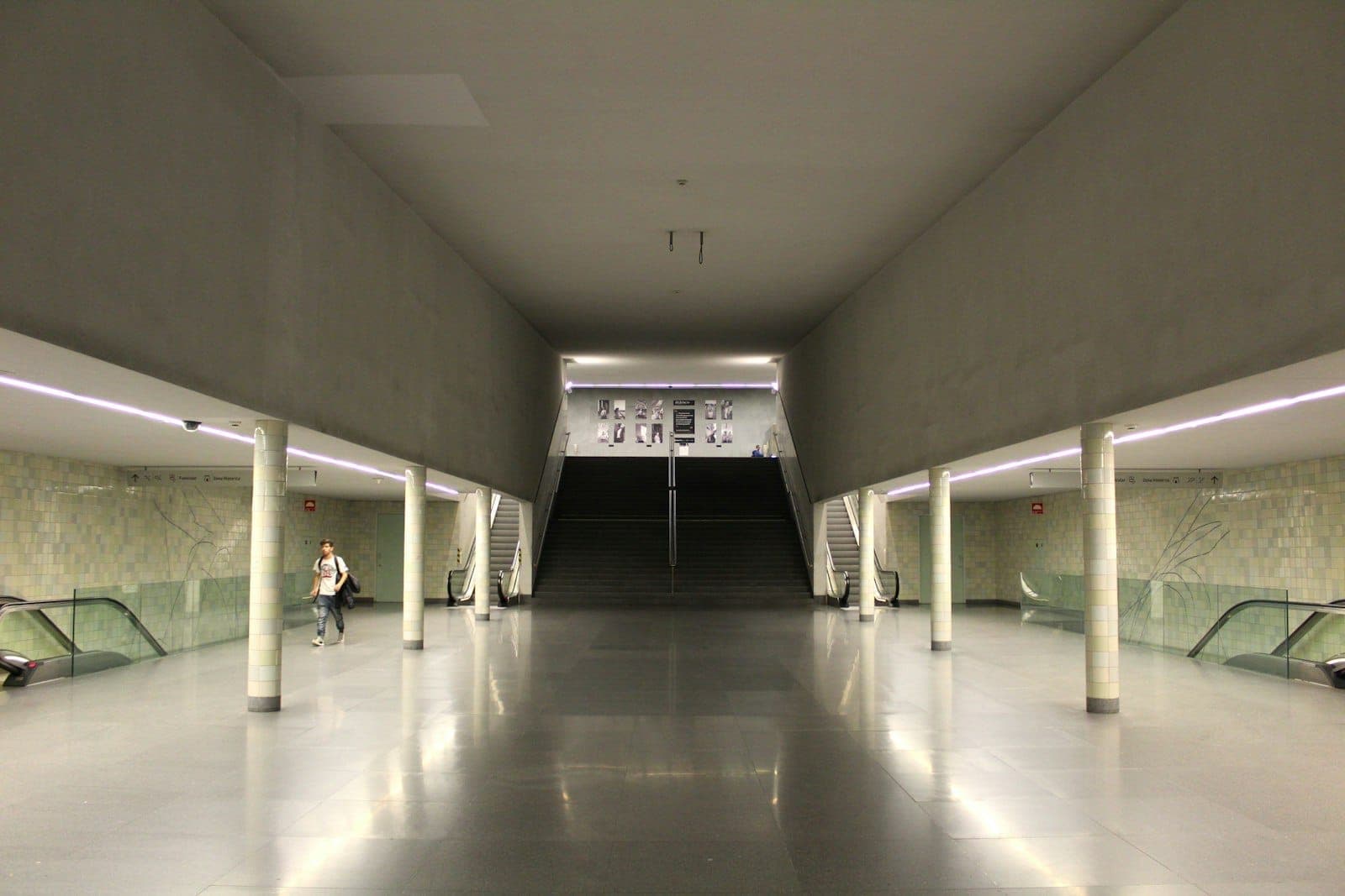 Innenraum eines modernen Verkehrsterminals in Porto mit Rolltreppen, Treppen und klarer Beschilderung, typisch für Ankunftsbereiche.