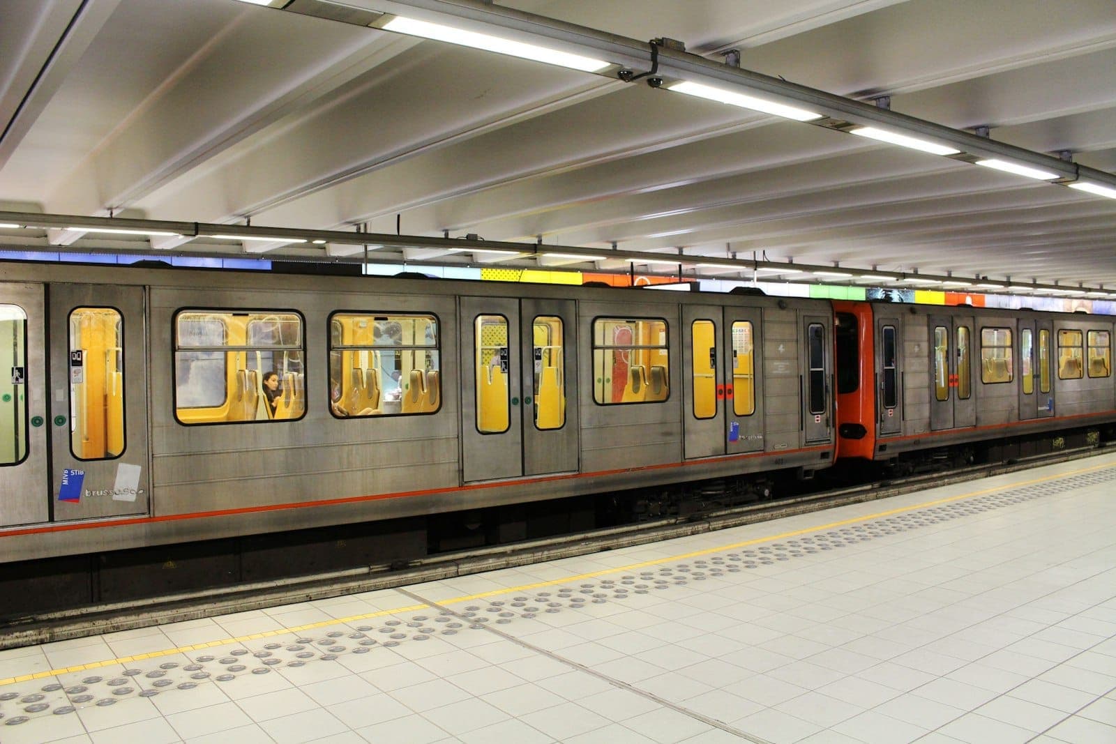 Moderner U-Bahn-Zug in einer gut beleuchteten unterirdischen Station mit sauberem Fliesenbahnsteig und farbiger Beschilderung über den Türen.