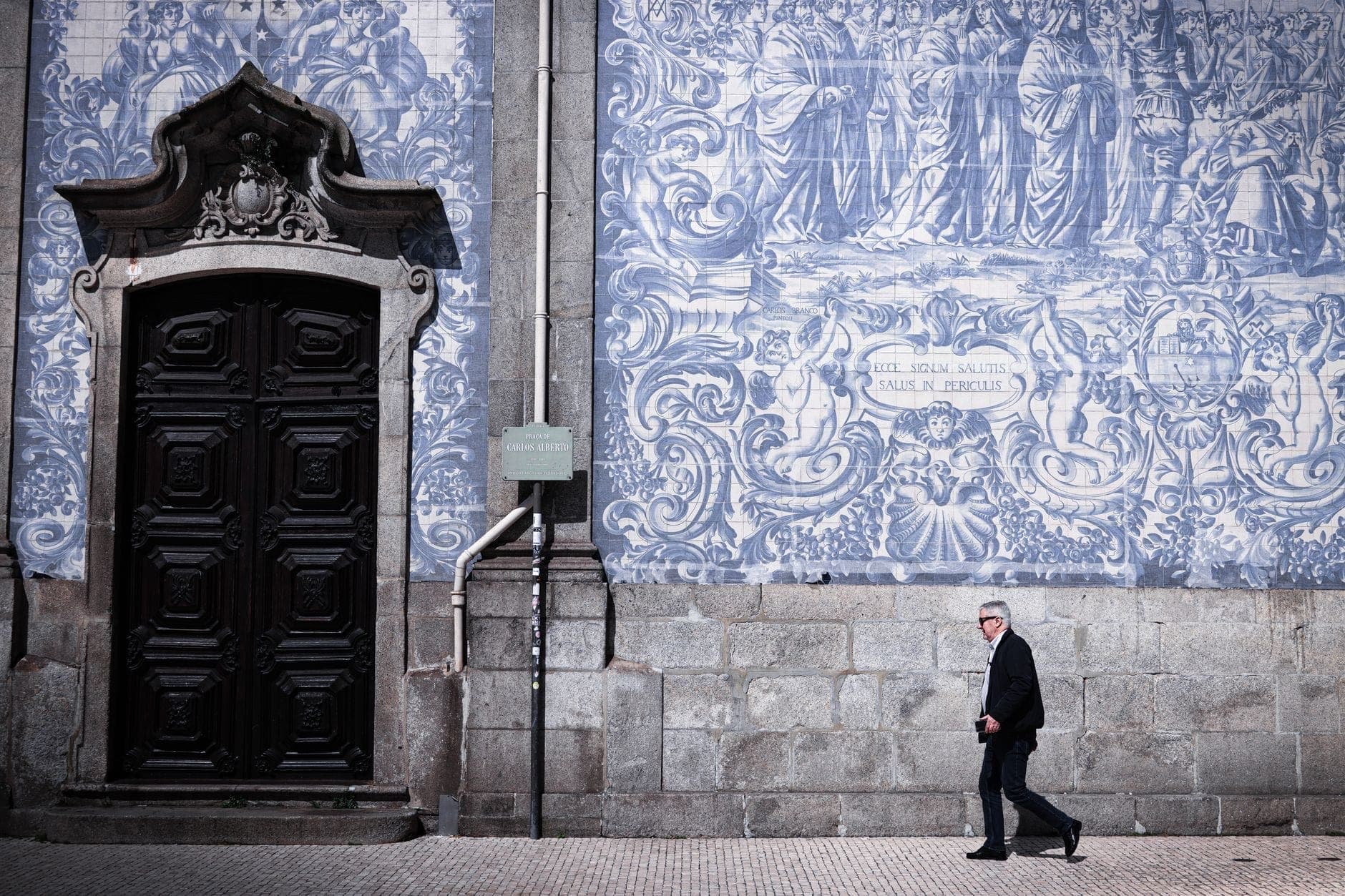 Homem a caminhar em frente à famosa fachada coberta de azulejos azuis e brancos de um edifício histórico no Porto, Portugal.
