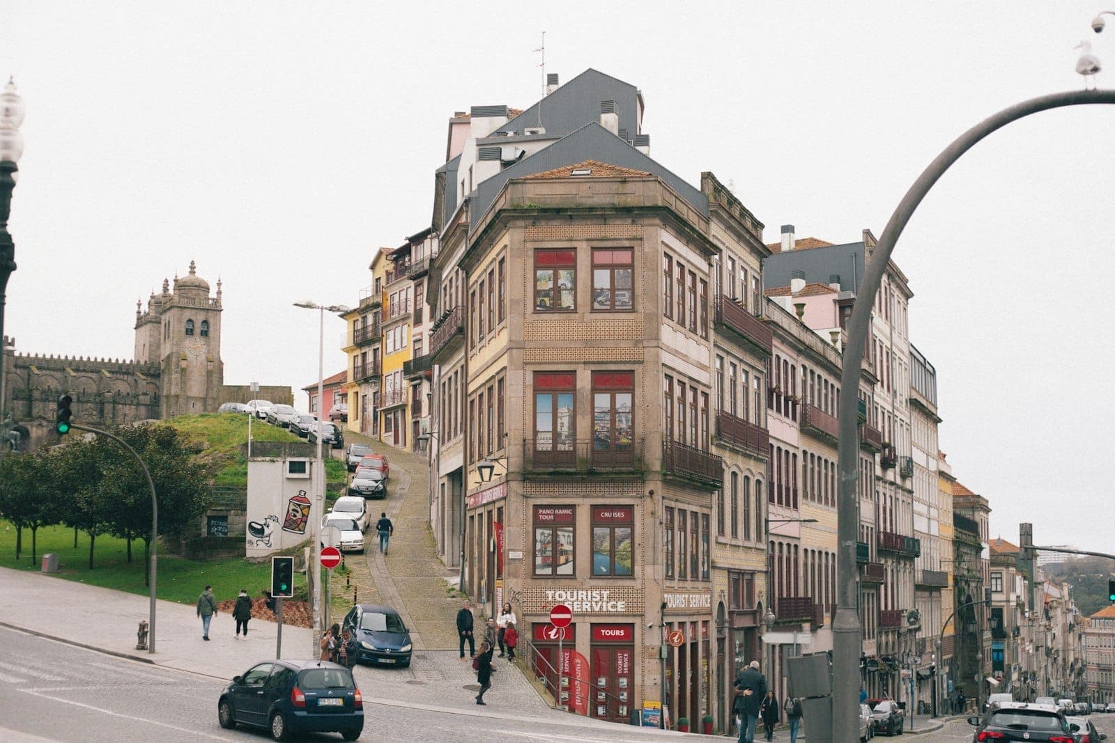 Ampla rua urbana no centro histórico do Porto com fachadas coloridas, pessoas a caminhar e a Catedral do Porto visível ao fundo.