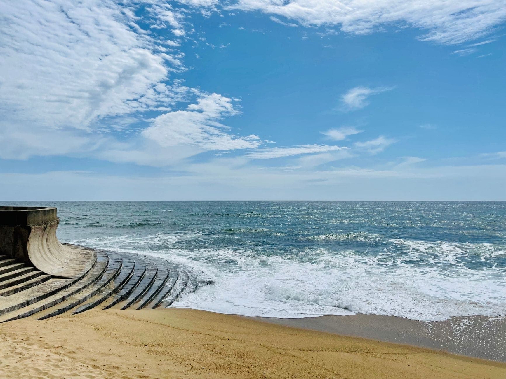 Modernistische Betonwand und Treppenstufen eines Schwimmbeckens, die sich unter blauem Himmel an der Küste von Porto in einen Sandstrand am Atlantik schmiegen