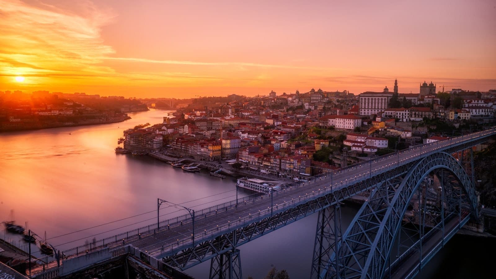 Die Brücke Dom Luís I in Porto bei Sonnenuntergang, die den Fluss Douro überspannt, mit der Skyline der Stadt und historischen Gebäuden im Hintergrund.
