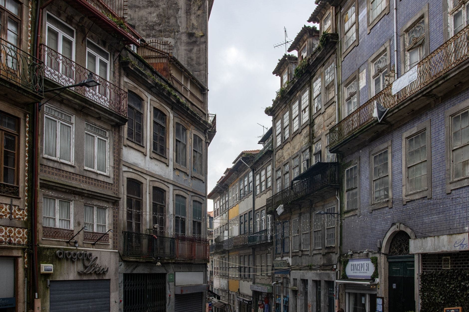Eine klassische enge Straße in Porto, gesäumt von historischen mehrstöckigen Gebäuden, viele mit Azulejo-Kacheln und Eisenbalkonen, die einen authentischen architektonischen Kontext widerspiegeln.