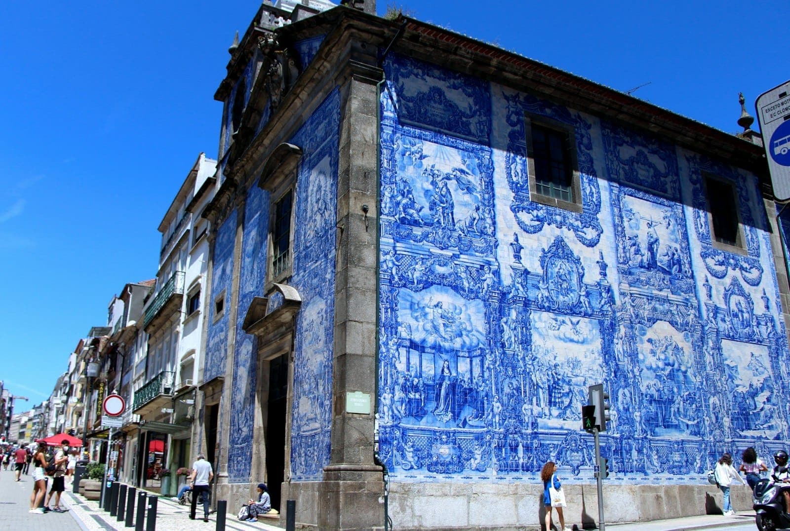 Eckansicht einer Kirche in Porto, die mit kunstvollen blau-weißen Azulejo-Kacheln bedeckt ist, mit Passanten an einem sonnigen Tag.