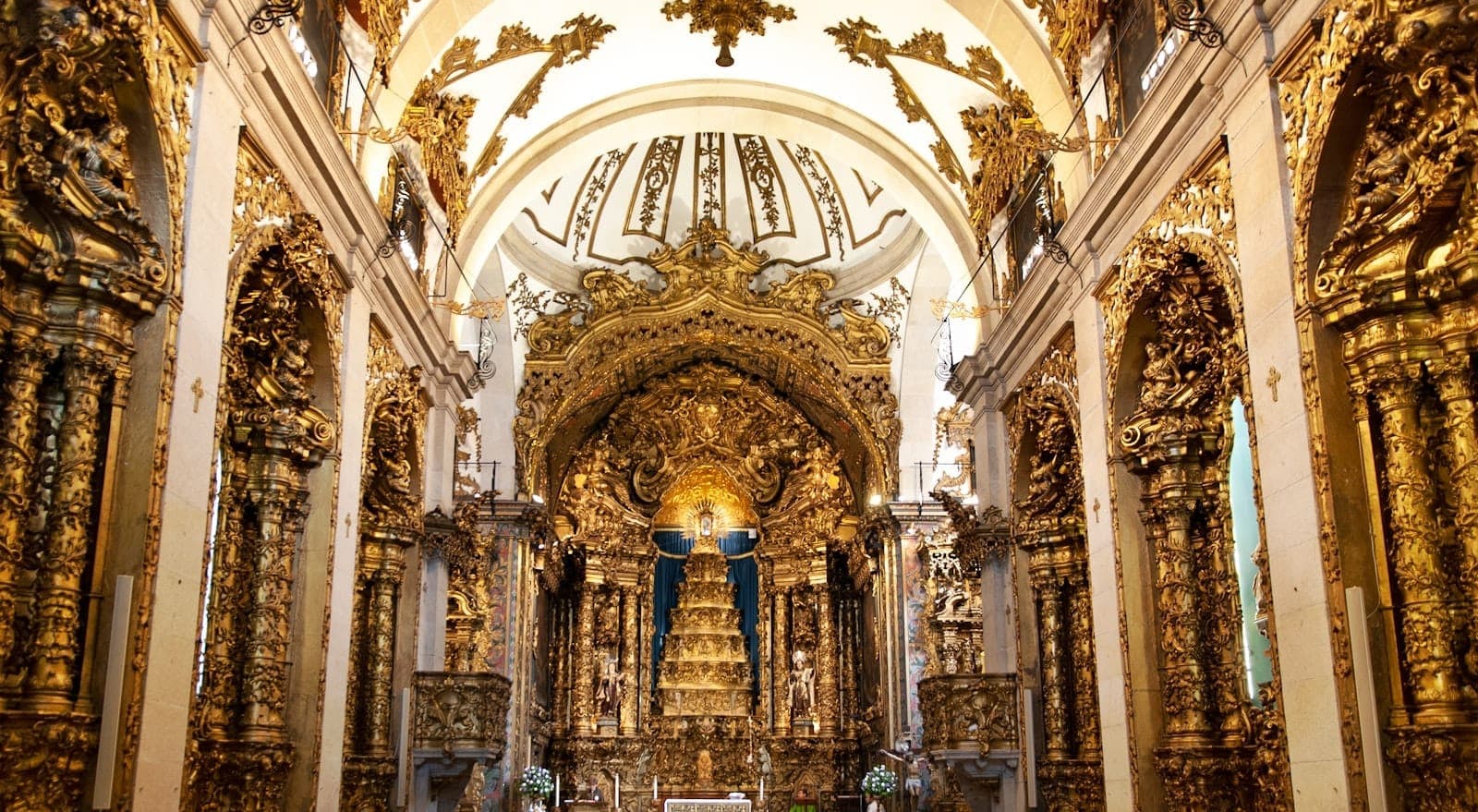 Prachtvoll dekoriertes Kircheninneres in Porto mit vergoldeten Barock-Holzschnitzereien und einem kunstvollen goldenen Altarbild unter hohen weißen Bögen.