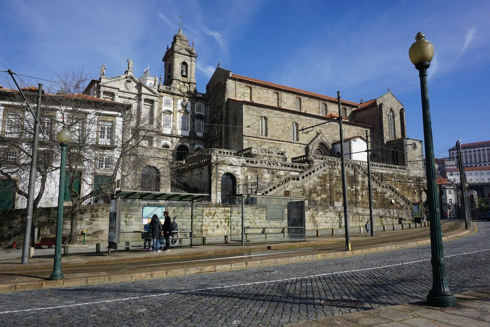 Weite Ansicht der Kathedrale von Porto mit ihren mittelalterlichen Steinmauern und einer Treppe, über der Straße an einem sonnigen Tag.