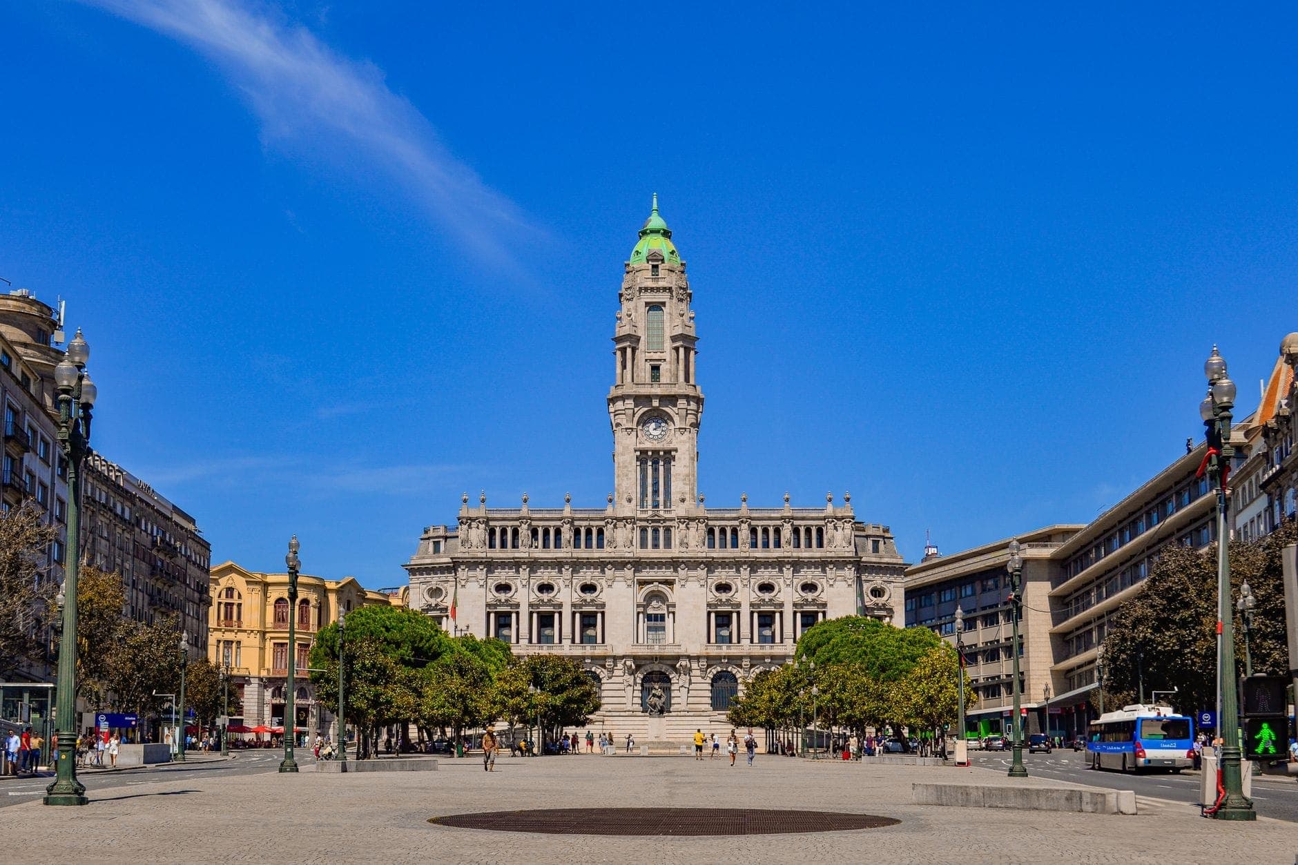 Ratusz Porto z wieżą zegarową w tle Avenida dos Aliados, sfotografowany w pogodny dzień na tle błękitnego nieba, z ludźmi na placu.