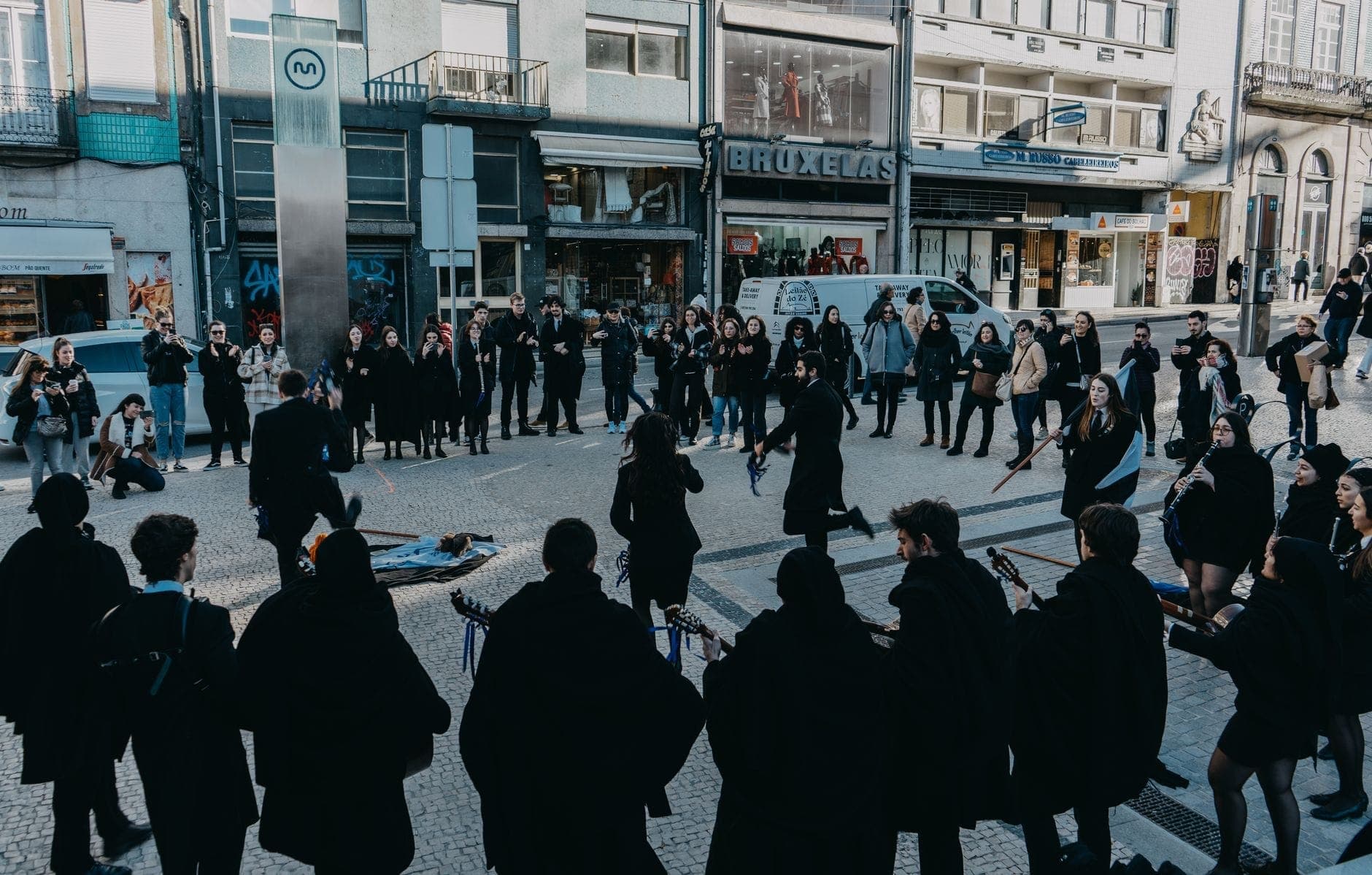 Un gruppo di musicisti e ballerini si esibisce in abiti neri tradizionali in una piazza centrale di Porto, circondato da spettatori e palazzi della città.