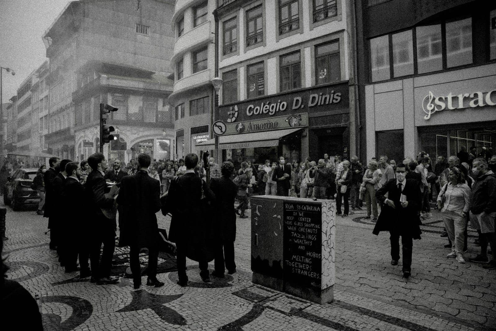 Musicisti di strada che si esibiscono in abiti neri su un affollato marciapiede di Porto, con una folla che guarda e negozi sullo sfondo.