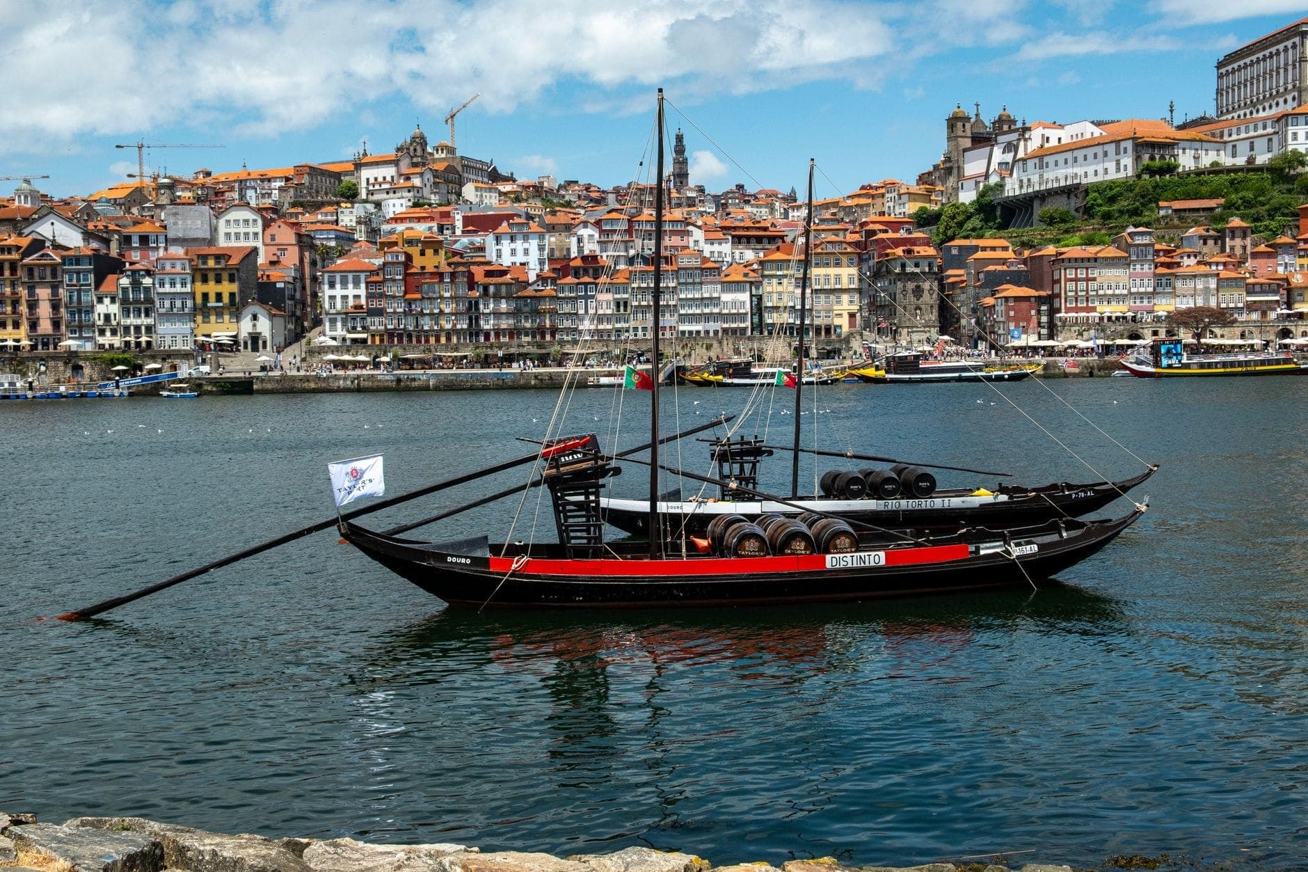 Tradizionale barca da vino di Porto con botti sul fiume Douro, skyline e lungofiume di Porto sullo sfondo sotto un cielo azzurro