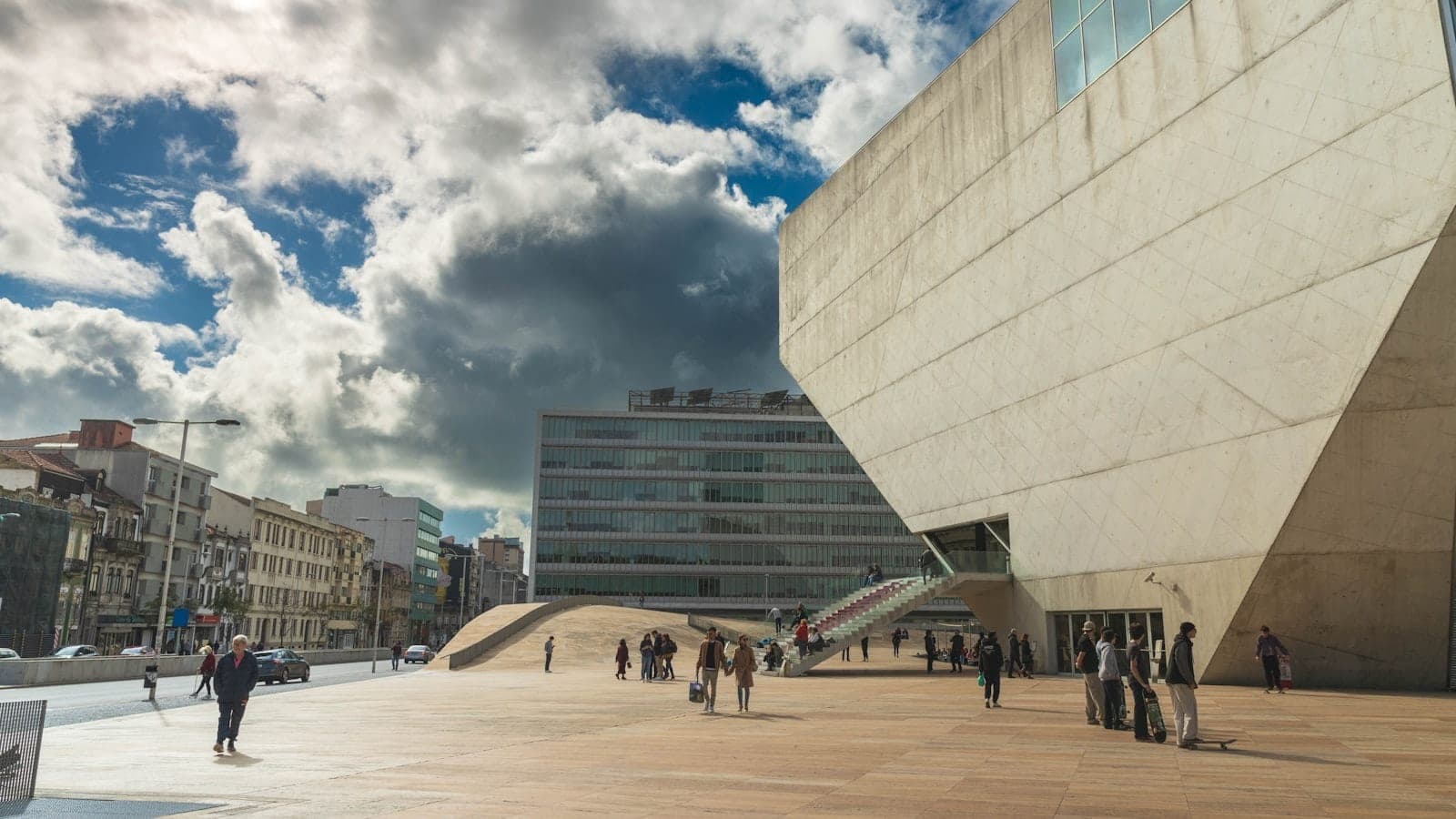 Edificio de arquitectura moderna en Oporto con personas caminando en una gran plaza abierta bajo un cielo dramático.