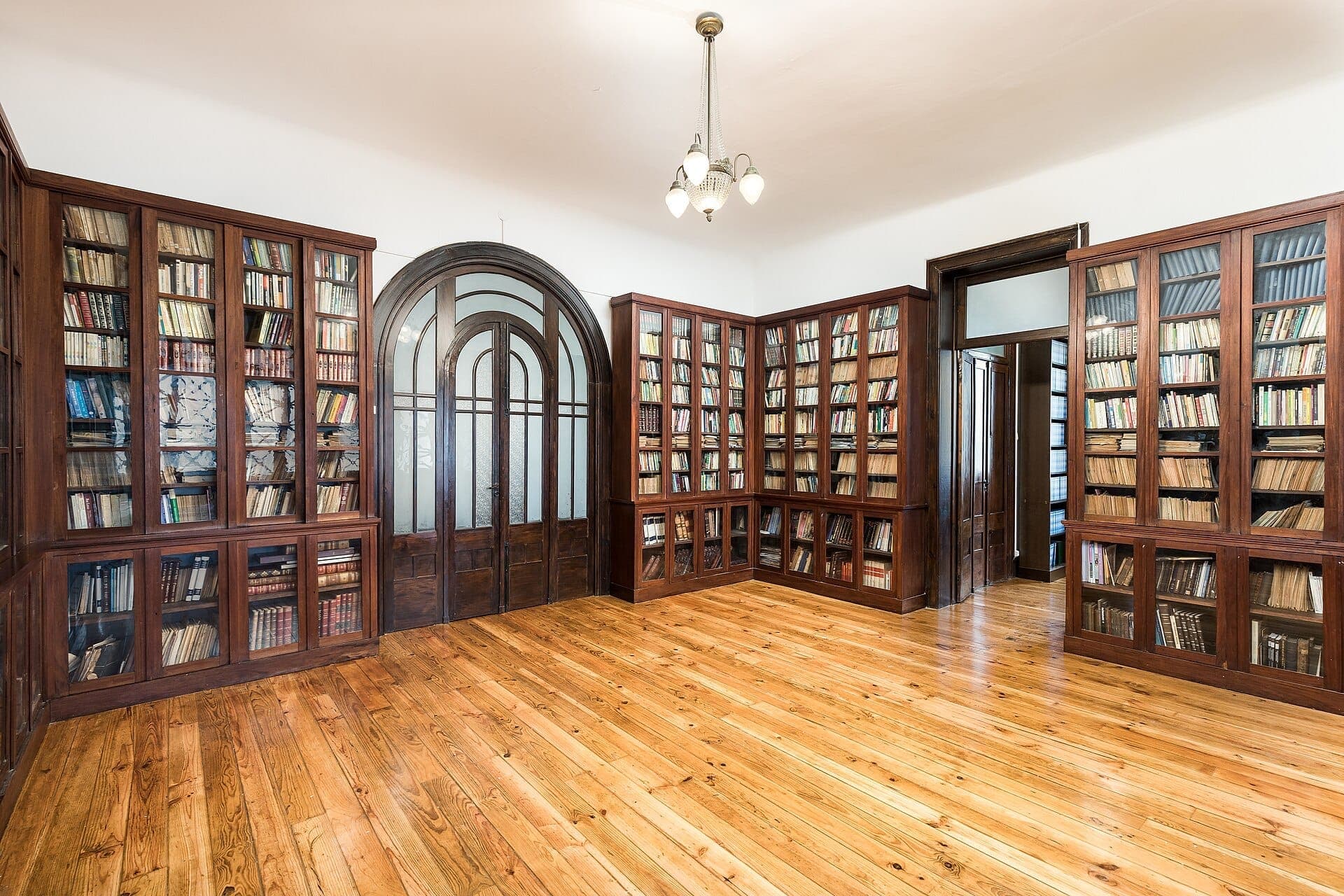 Geräumiger, gut beleuchteter Raum im Inneren des Porto Jewish Museum mit hölzernen Bücherregalen voller Bücher, polierten Holzböden und gewölbten Glastüren.