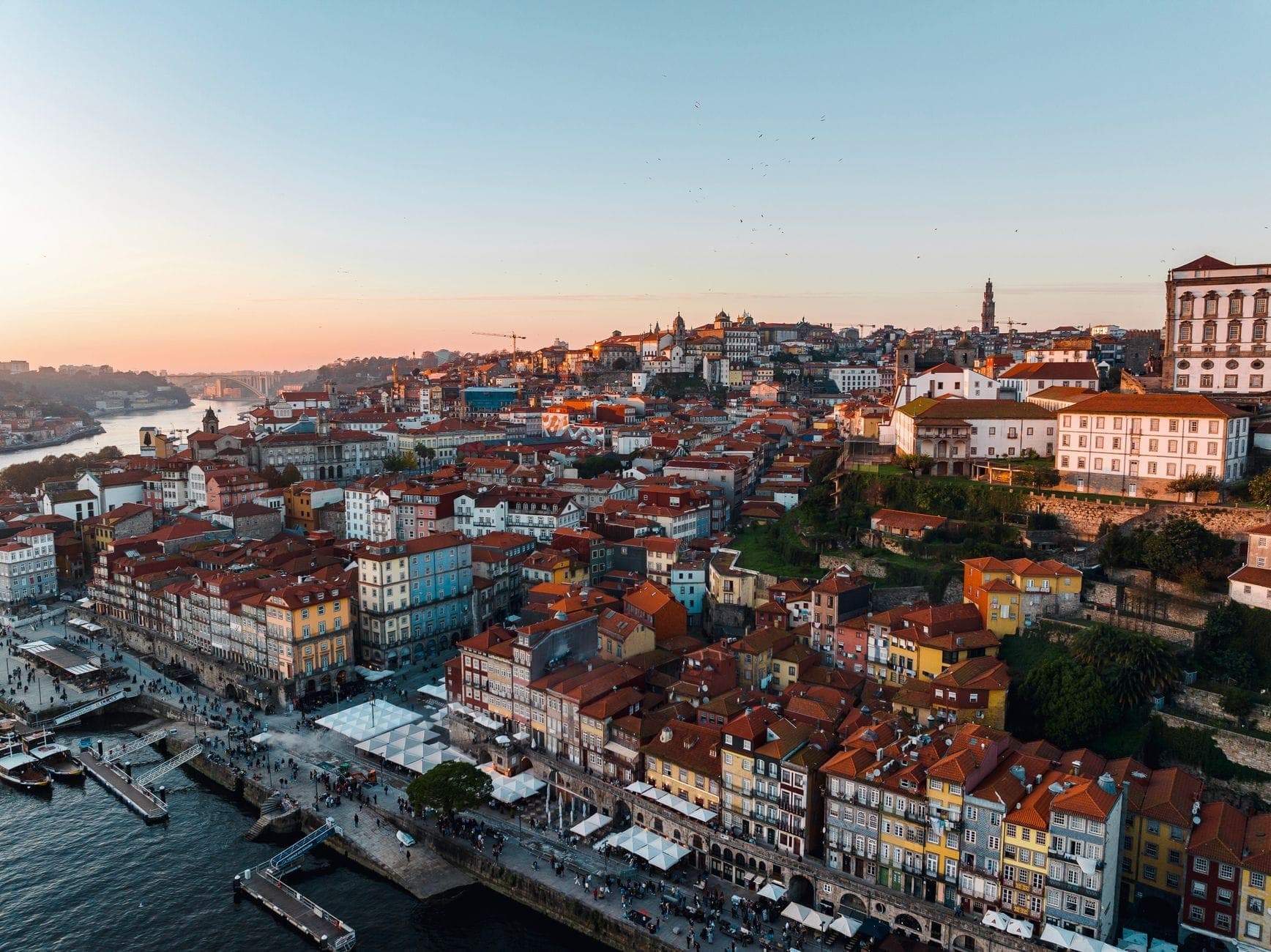 Kolorowe tradycyjne budynki nad rzeką i ruchoma promenada wzdłuż rzeki Douro w Porto o zachodzie słońca, ukazujące zwarte i tętniące życiem historyczne centrum miasta.