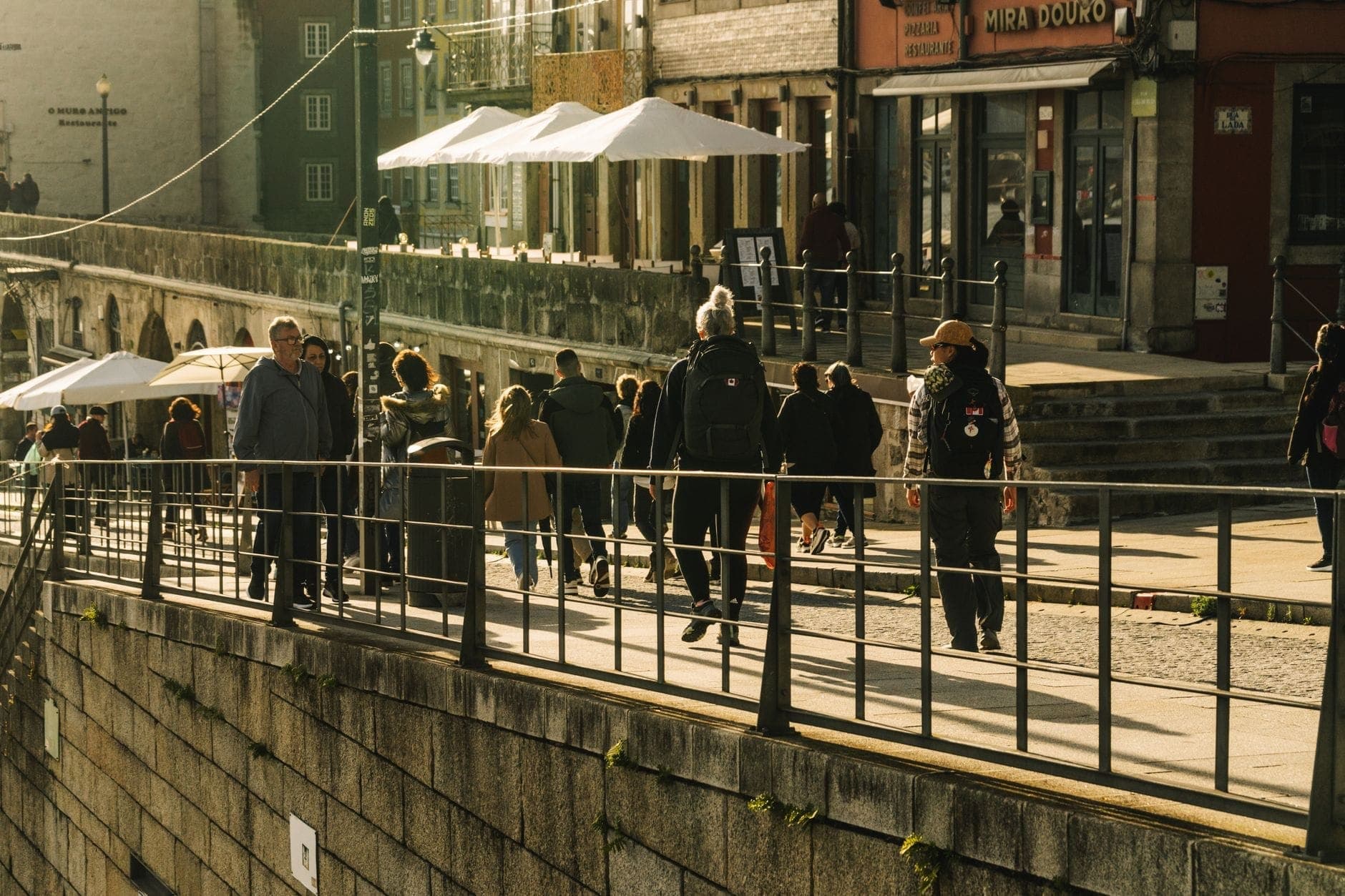 Pessoas caminhando pelo animado calçadão à beira-mar do Porto, com edifícios históricos e cafés ao ar livre visíveis.