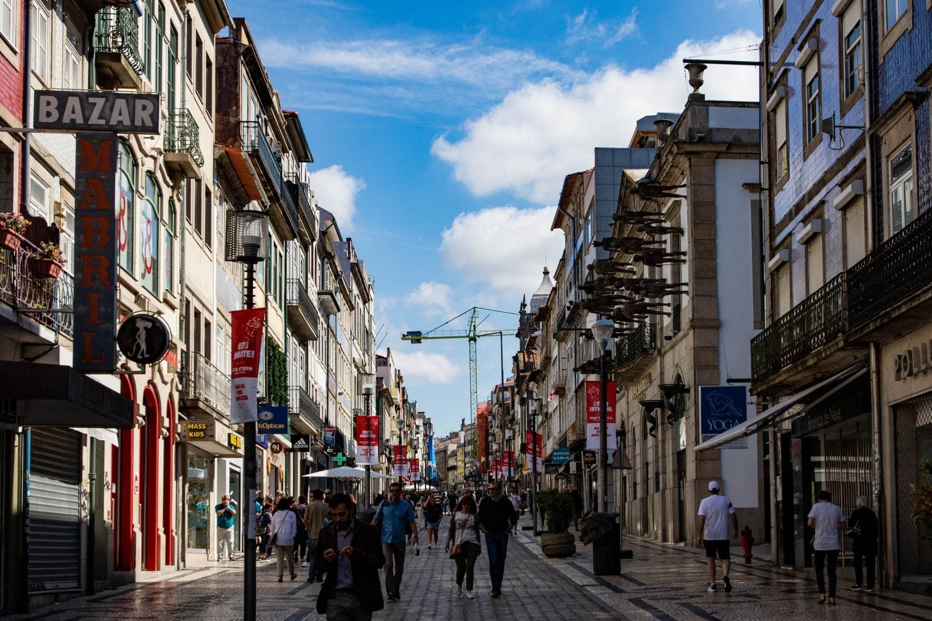 Belebte Einkaufsstraße in Porto mit bunten traditionellen Gebäuden, Geschäften und Menschen, die unter einem strahlend blauen Himmel spazieren.
