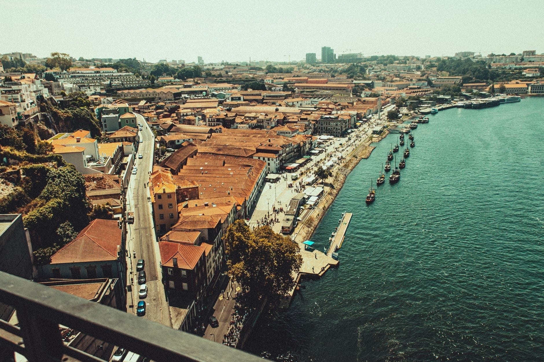 Uferpromenade von Vila Nova de Gaia mit Portwein-Kellereien, Booten auf dem Fluss Douro und der Stadtsilhouette im hellen Tageslicht.