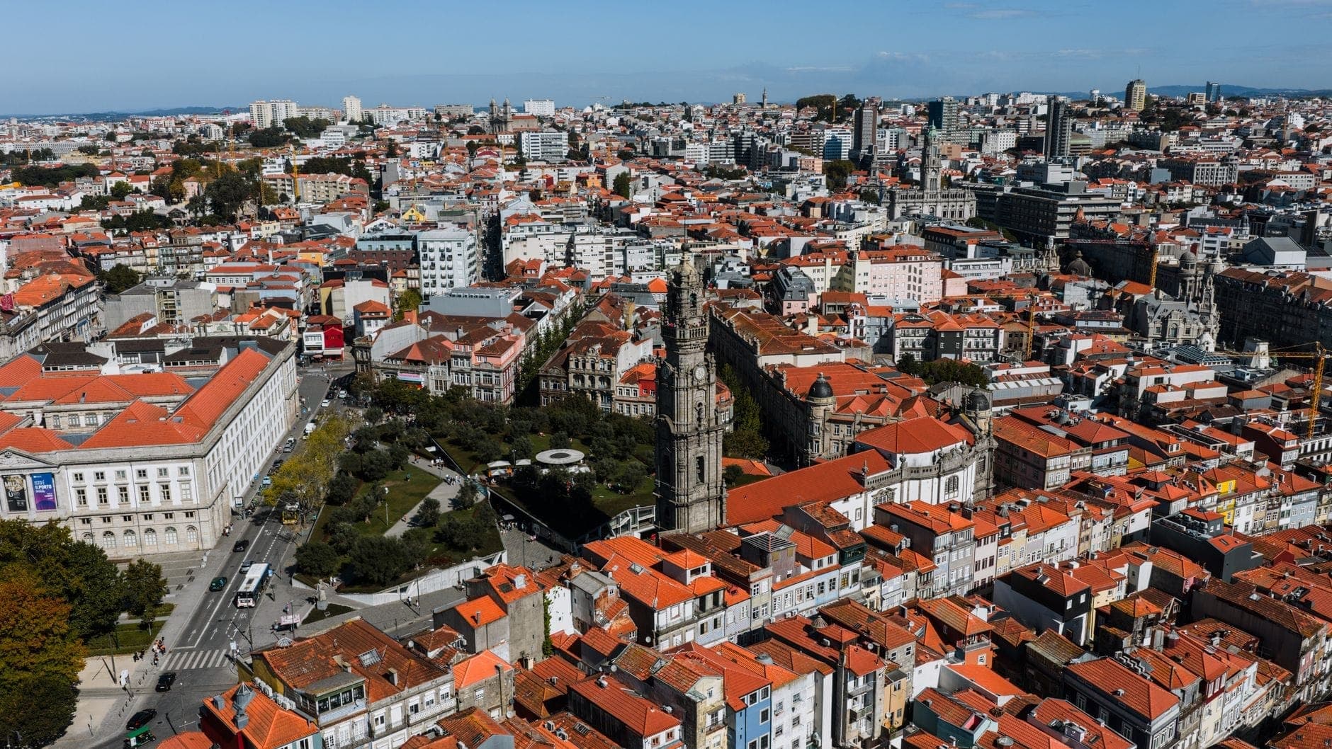 Widok z lotu ptaka na Porto z gęstym historycznym centrum, ikoniczną Torre dos Clérigos, dachówkowymi dachami i zwartymi uliczkami nadającymi się do spacerów pod bezchmurnym błękitnym niebem.