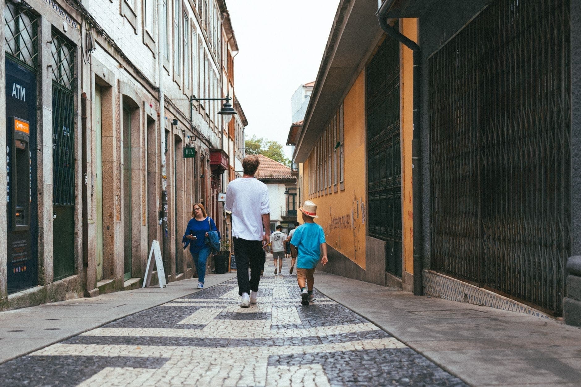 Una famiglia passeggia lungo una pittoresca strada acciottolata di Porto, con adulti e bambini che esplorano colorati edifici storici in una giornata di sole.