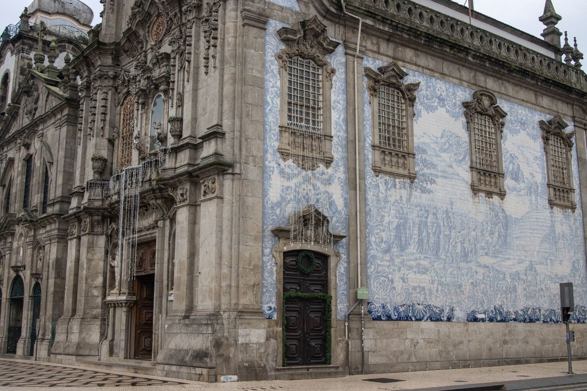 Igreja barroca histórica no Porto com uma fachada elaborada e um grande mural de azulejos azuis e brancos, vista da esquina da rua.
