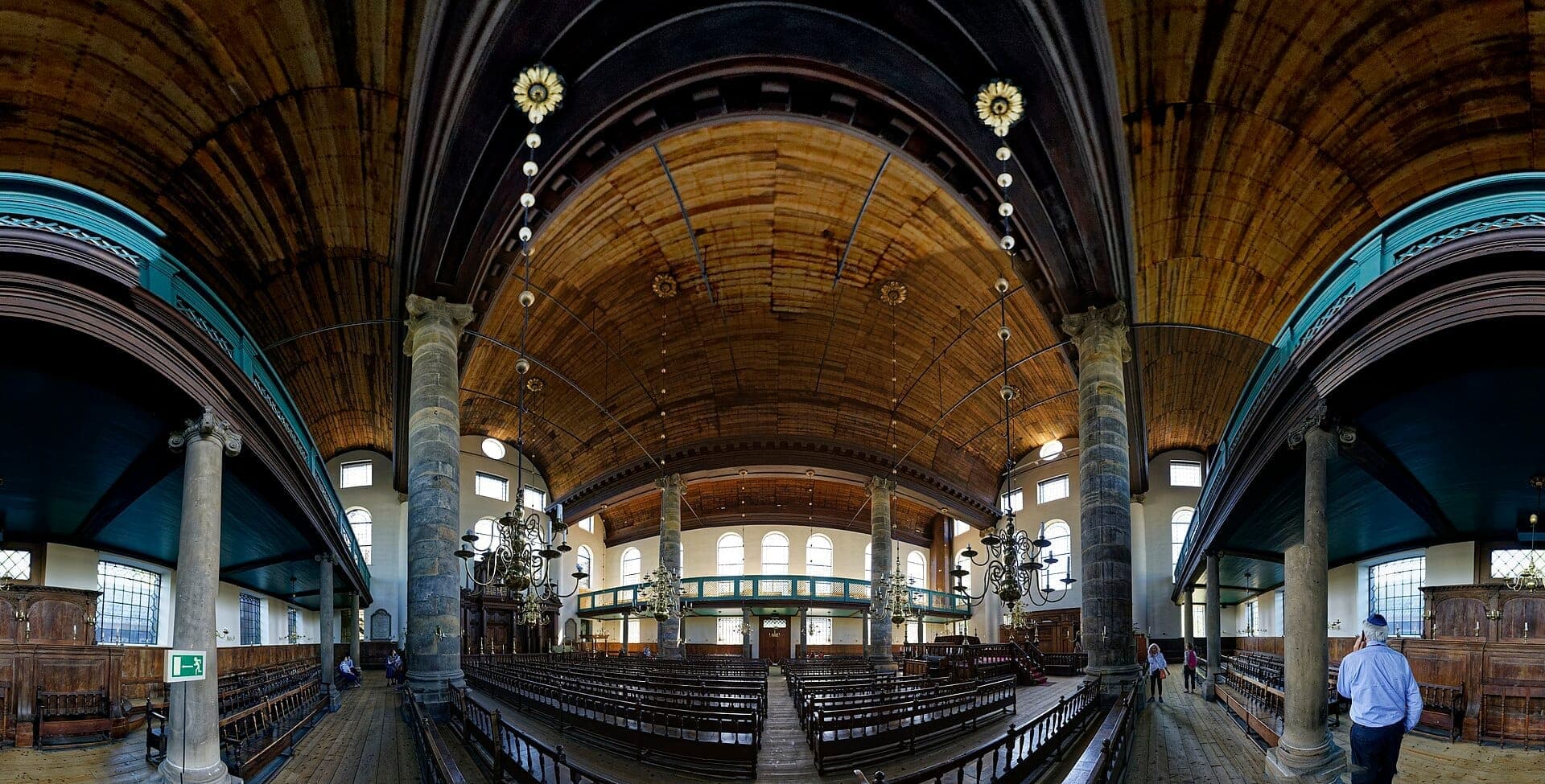 Weitwinkelansicht des Innenraums der Portugiesischen Synagoge Amsterdam mit gewölbter Holzdecke, Steinsäulen, Kronleuchtern und Holzbänken im natürlichen Licht.