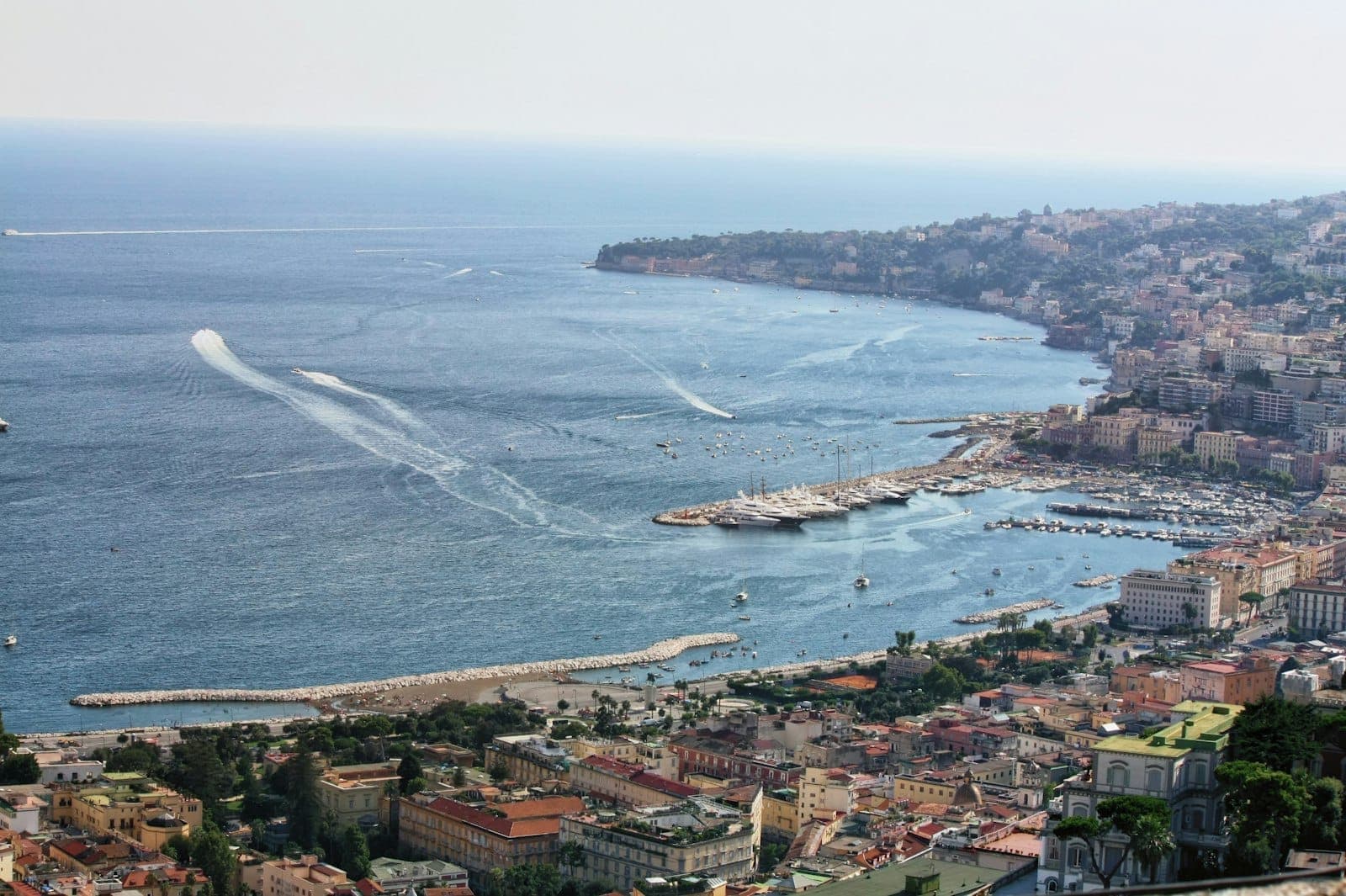 Vista aérea panorâmica do litoral de Posillipo, com falésias de calcário, vilas à beira-mar, marinas e a curva do exclusivo bairro costeiro de Nápoles.