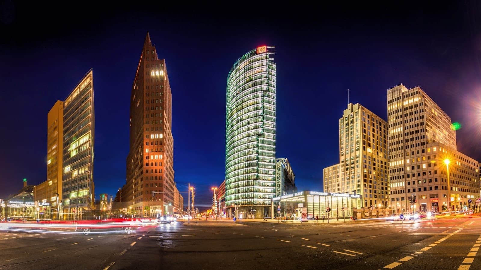 ภาพมุมกว้างยามค่ำของ Potsdamer Platz ตึกสูงสมัยใหม่ส่องไฟสว่างตัดกับท้องฟ้ายามราตรี เส้นไฟจราจรและชีวิตชีวาในเบอร์ลิน