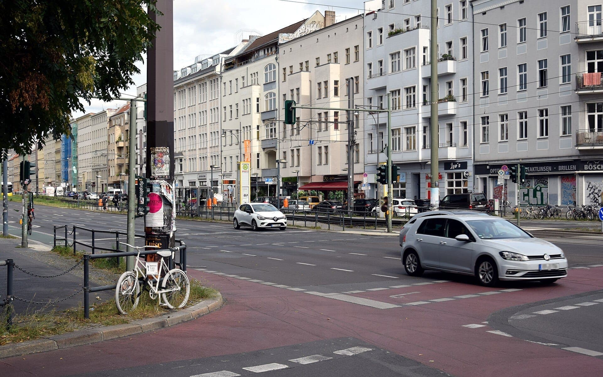 วิวถนนกว้างใน Prenzlauer Berg, เบอร์ลิน แสดงให้เห็นอาคารอพาร์ตเมนต์สไตล์คลาสสิก รถยนต์ จักรยาน และต้นไม้ใบเขียวในวันที่มีเมฆมาก